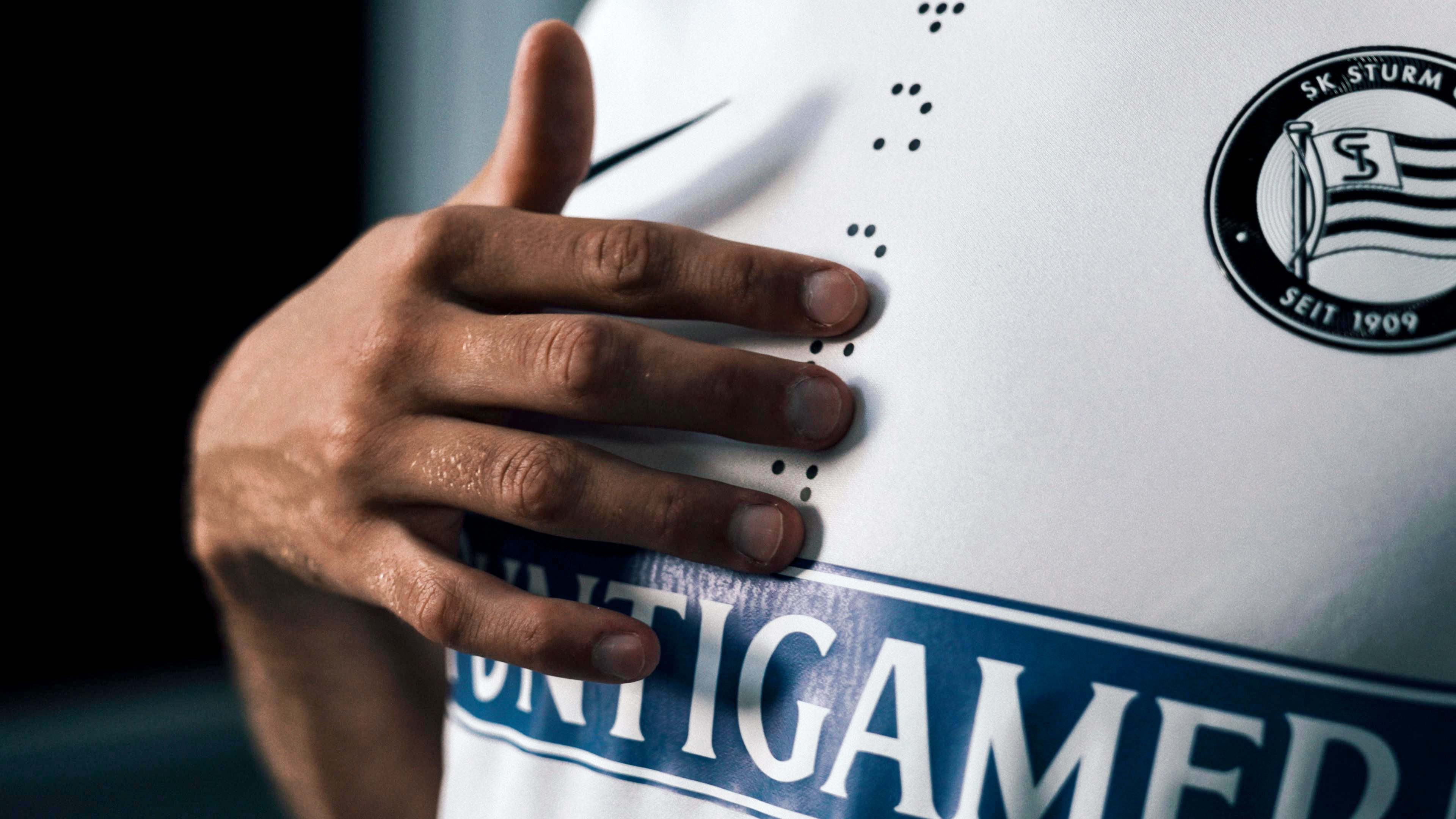 Eine Hand berührt Blindenschrift-Punkte auf einem weißen Trikot