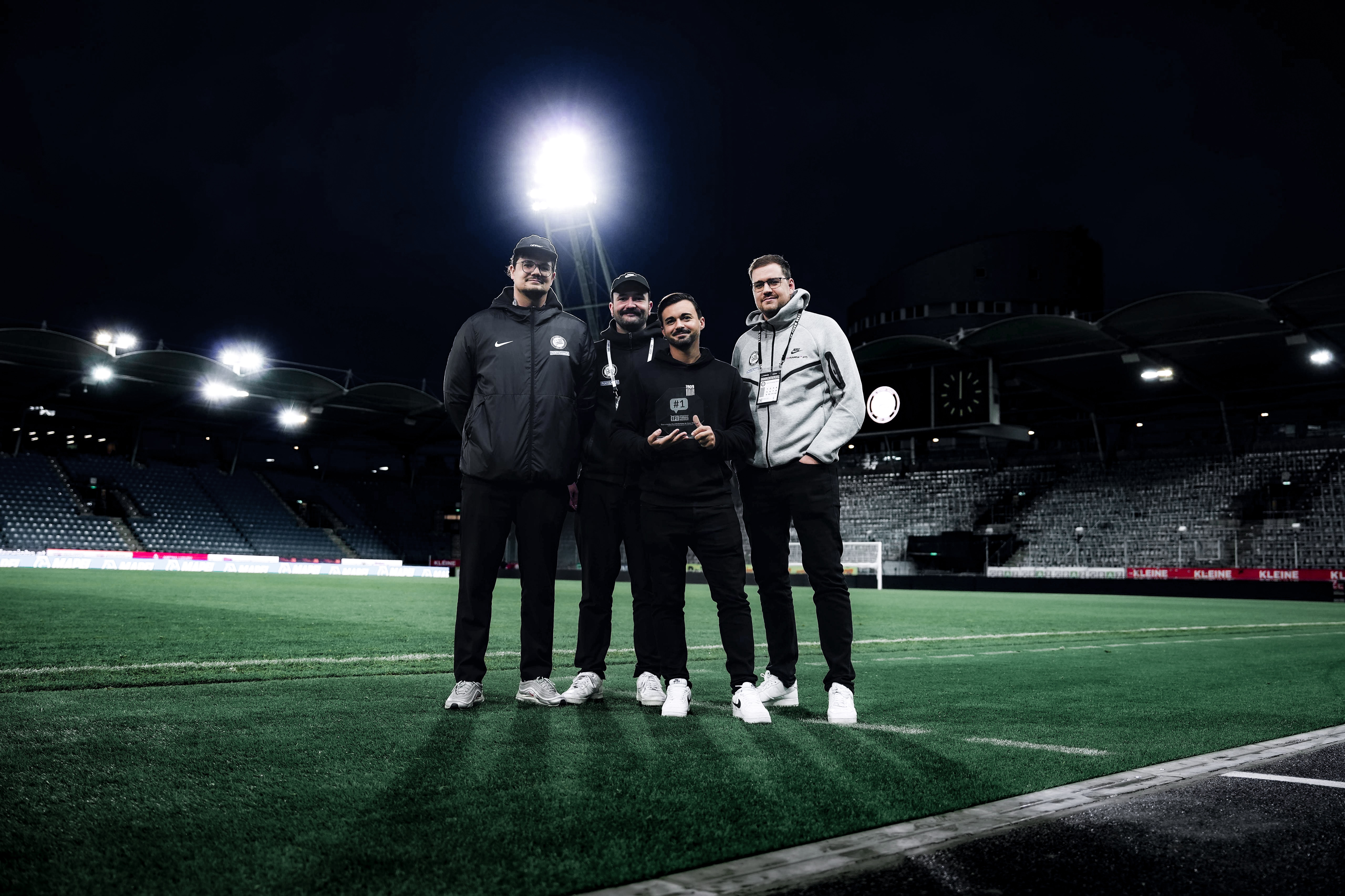 Vier Männer stehen am Fußballfeld und halten eine Trophäe in den Händen