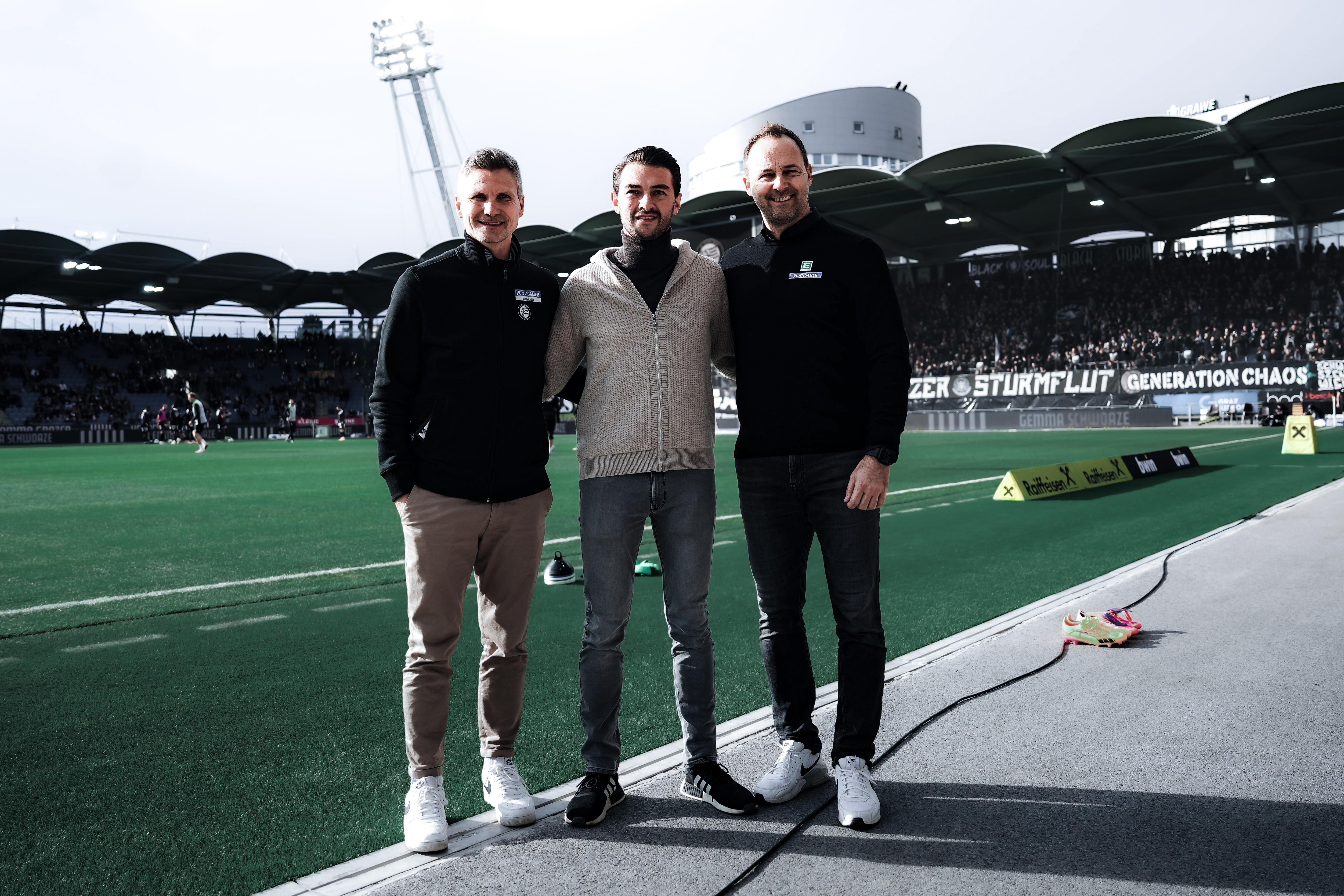 Drei Männer stehen neben dem Fußballplatz.