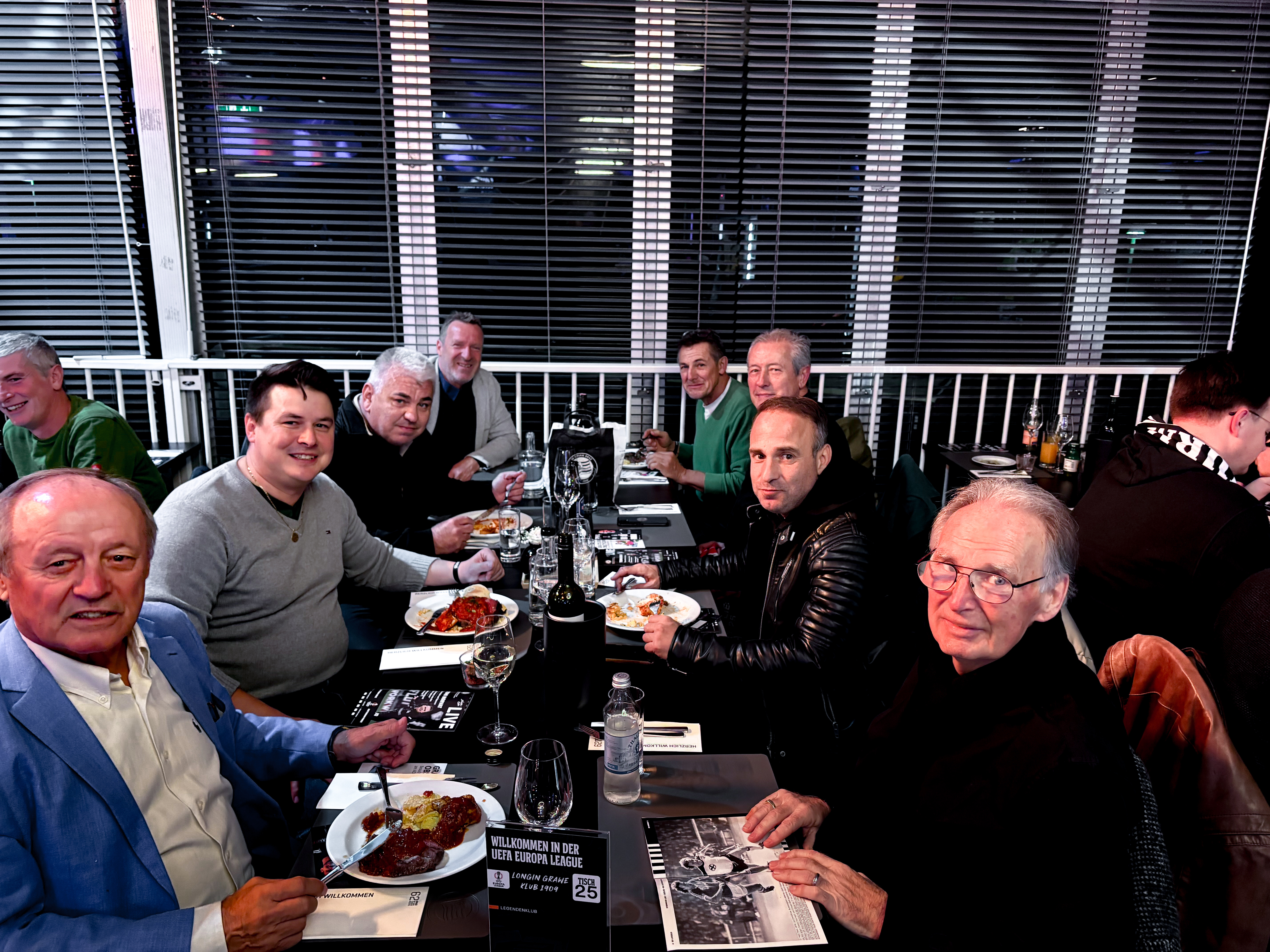 Acht Männer sitzen an einem Tisch und essen.