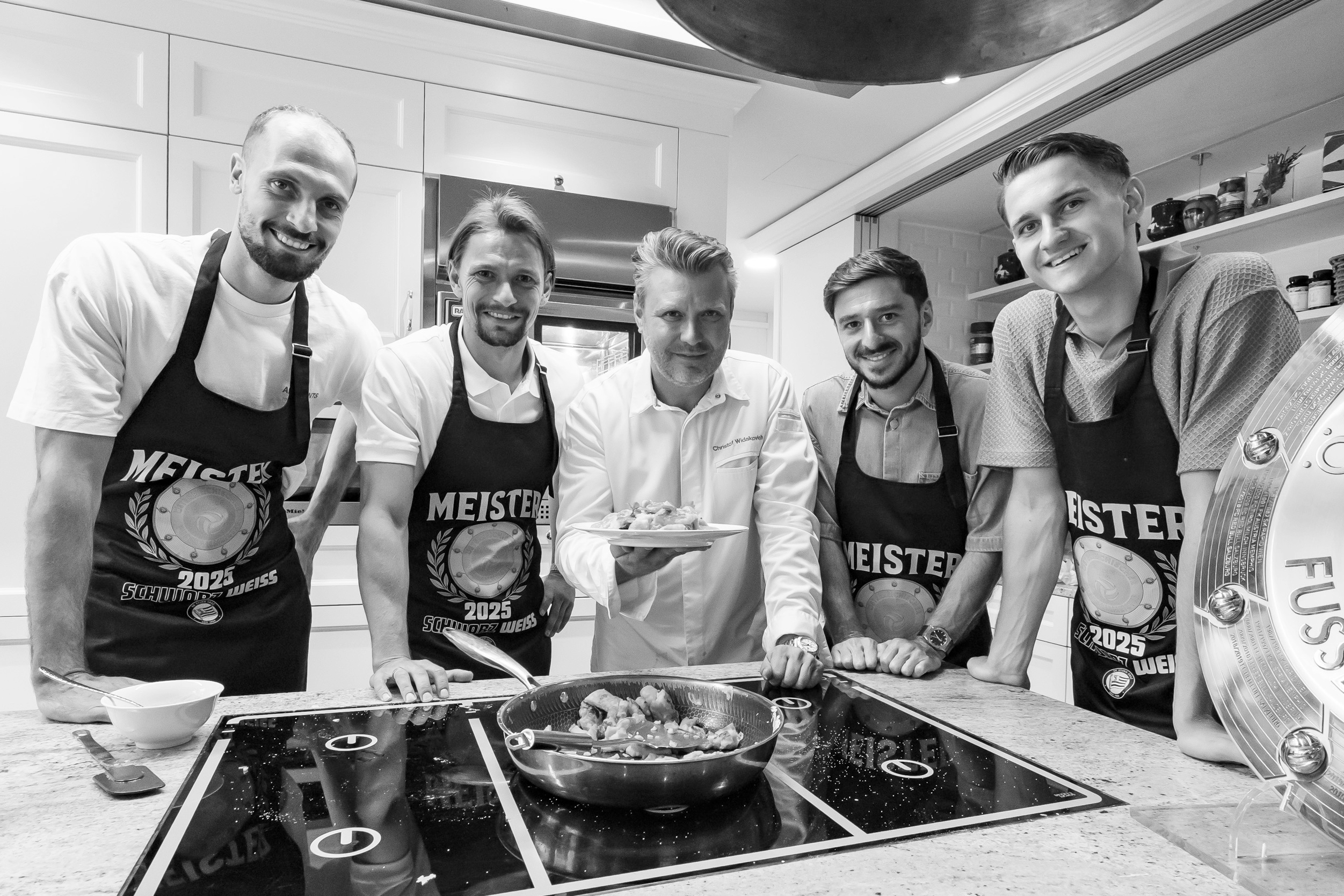 Vier Fußballer und ein Koch stehen am Herd und bewundern ihr Werk.