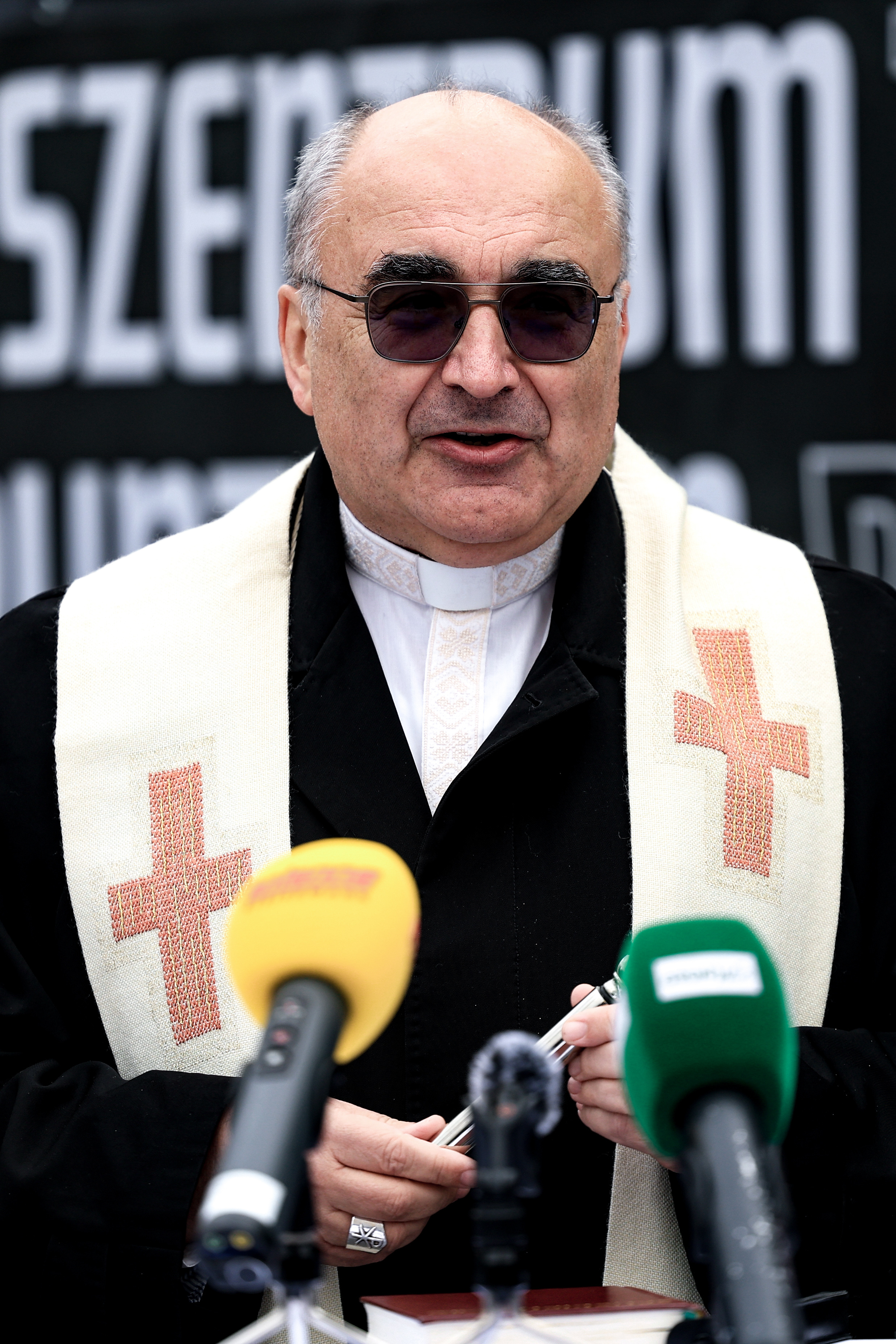 Ein Priester mit Sonnenbrille spricht in Mikrofone