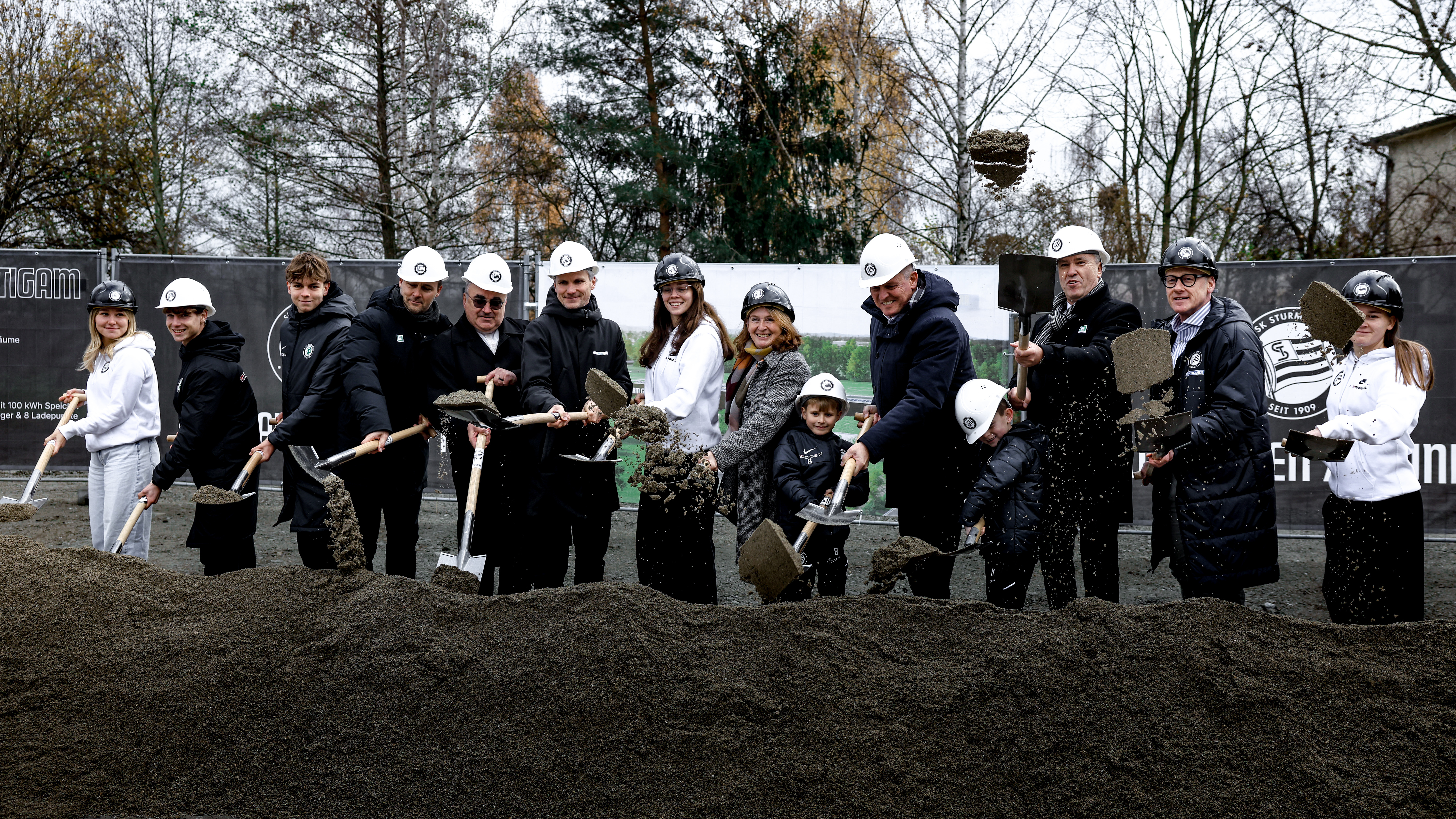 Gruppe an Personen schaufelt symbolisch Erde an einer Baustelle