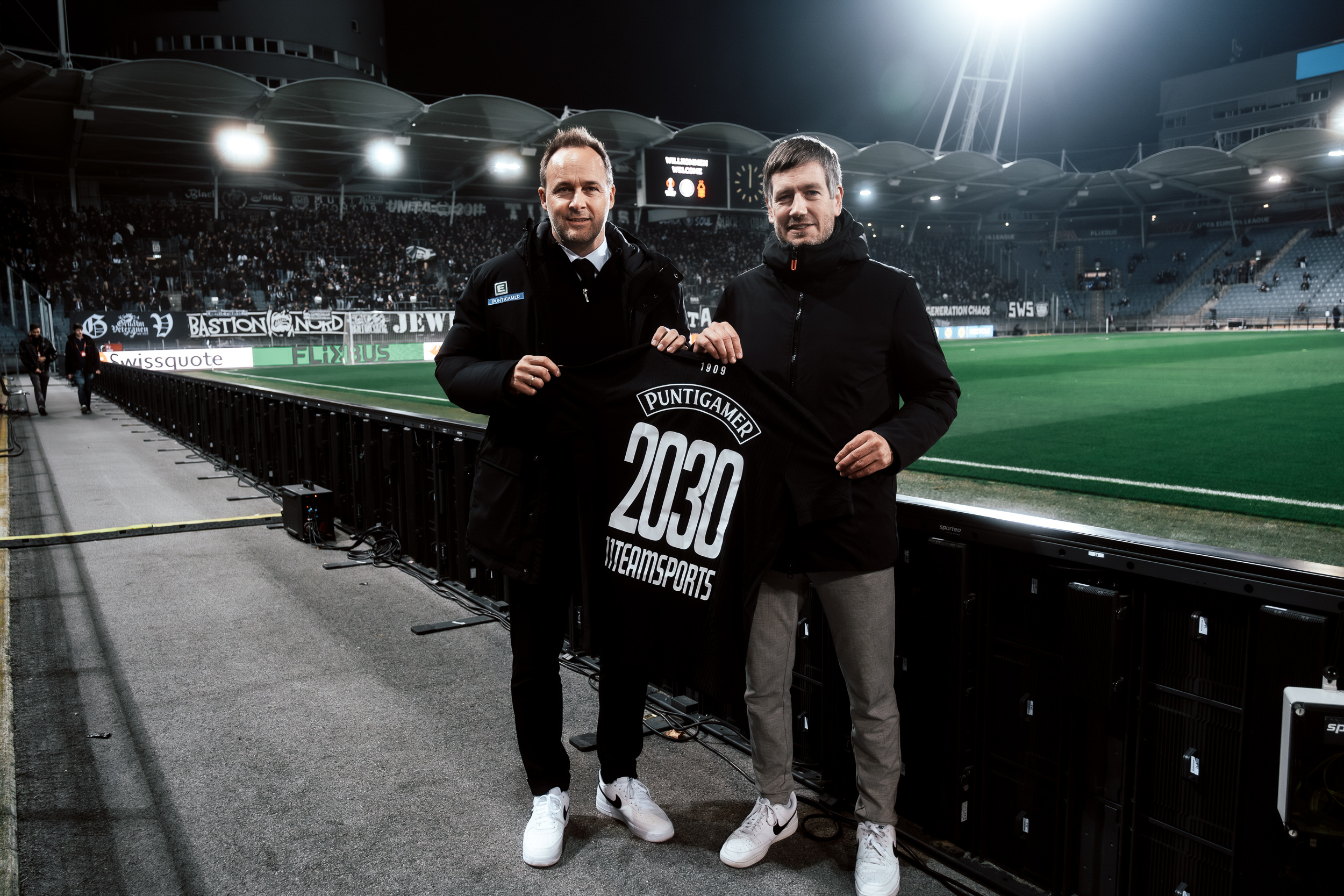 Zwei Männer stehen im Stadion und halten ein Trikot