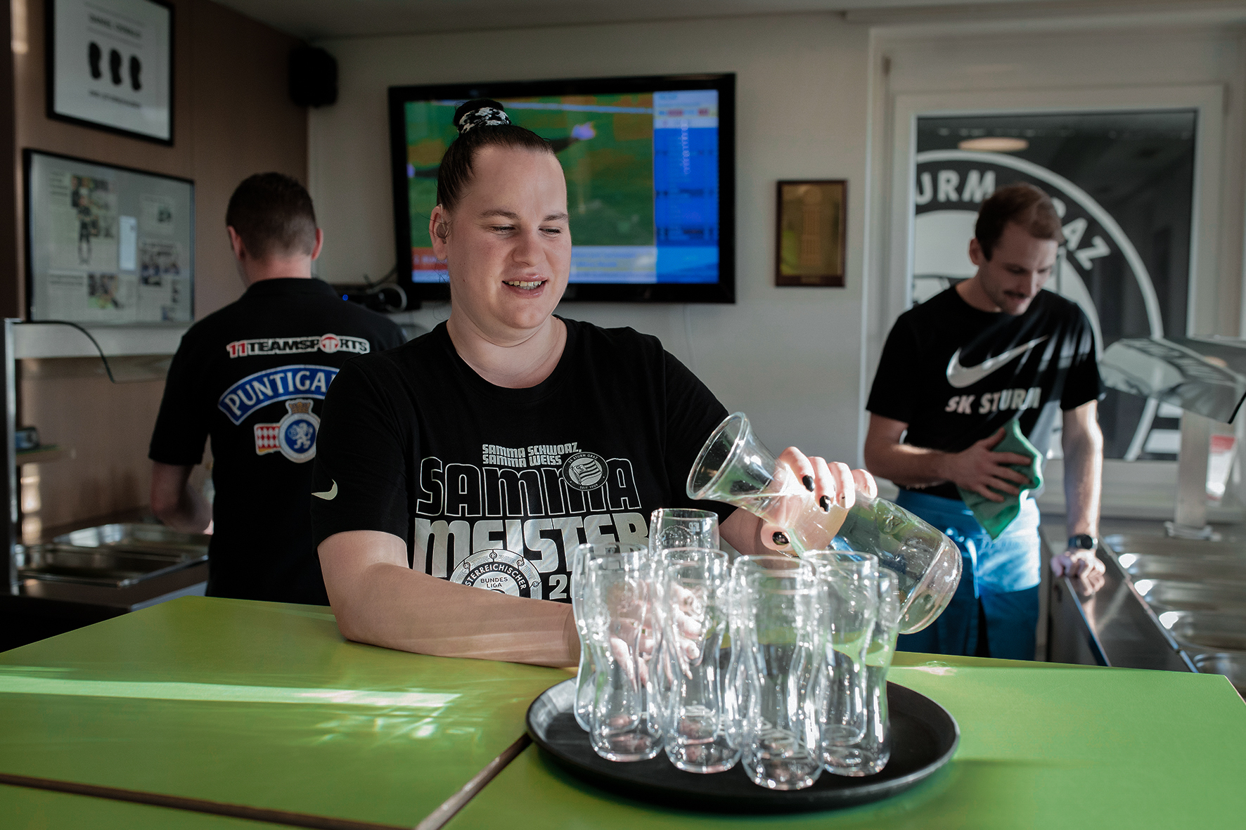 Eine Frau schüttet Wasser aus einem Krug in Gläser auf einem Tablett.