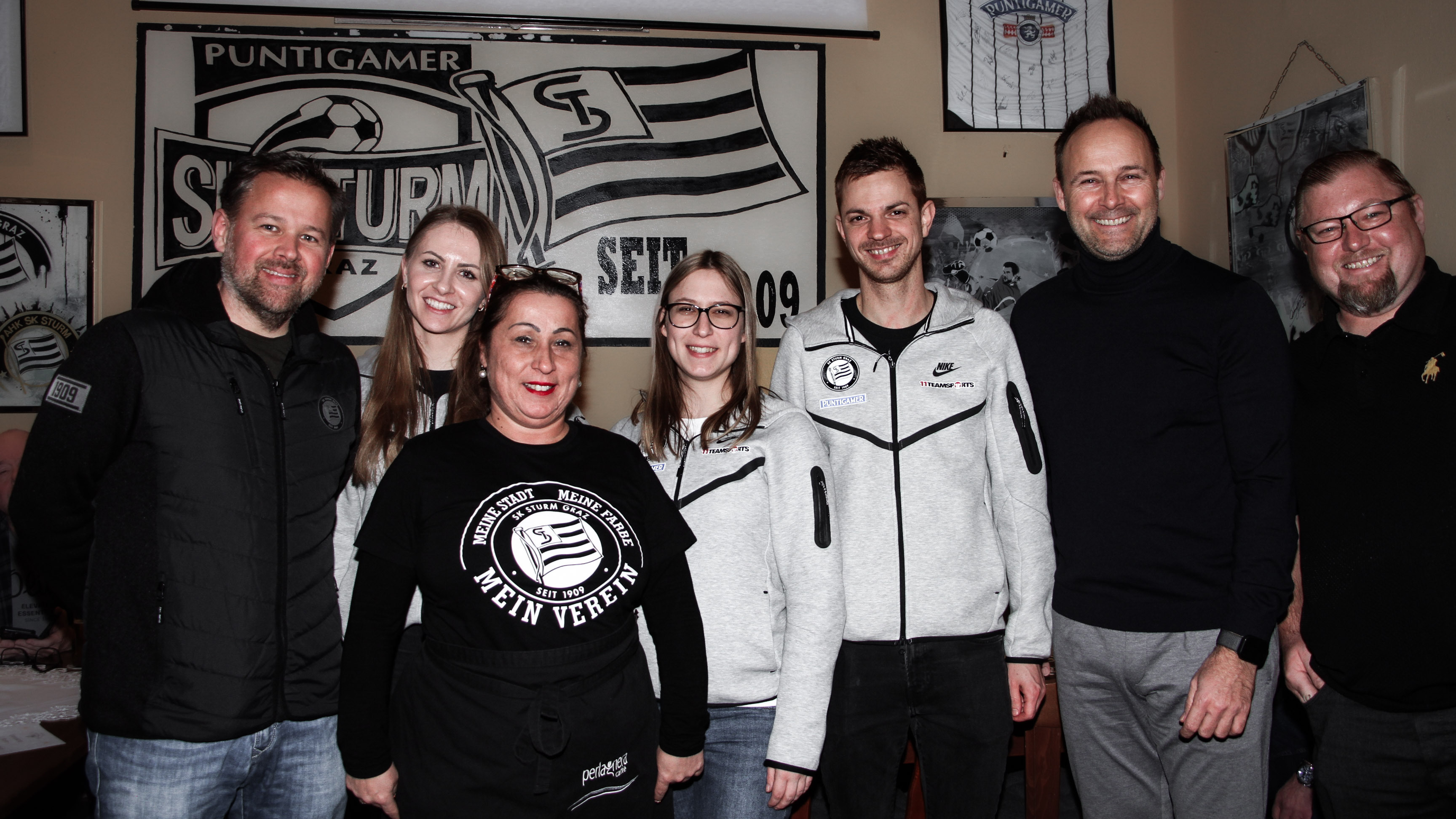 Vier Männer und drei Frauen schauen zur Kamera