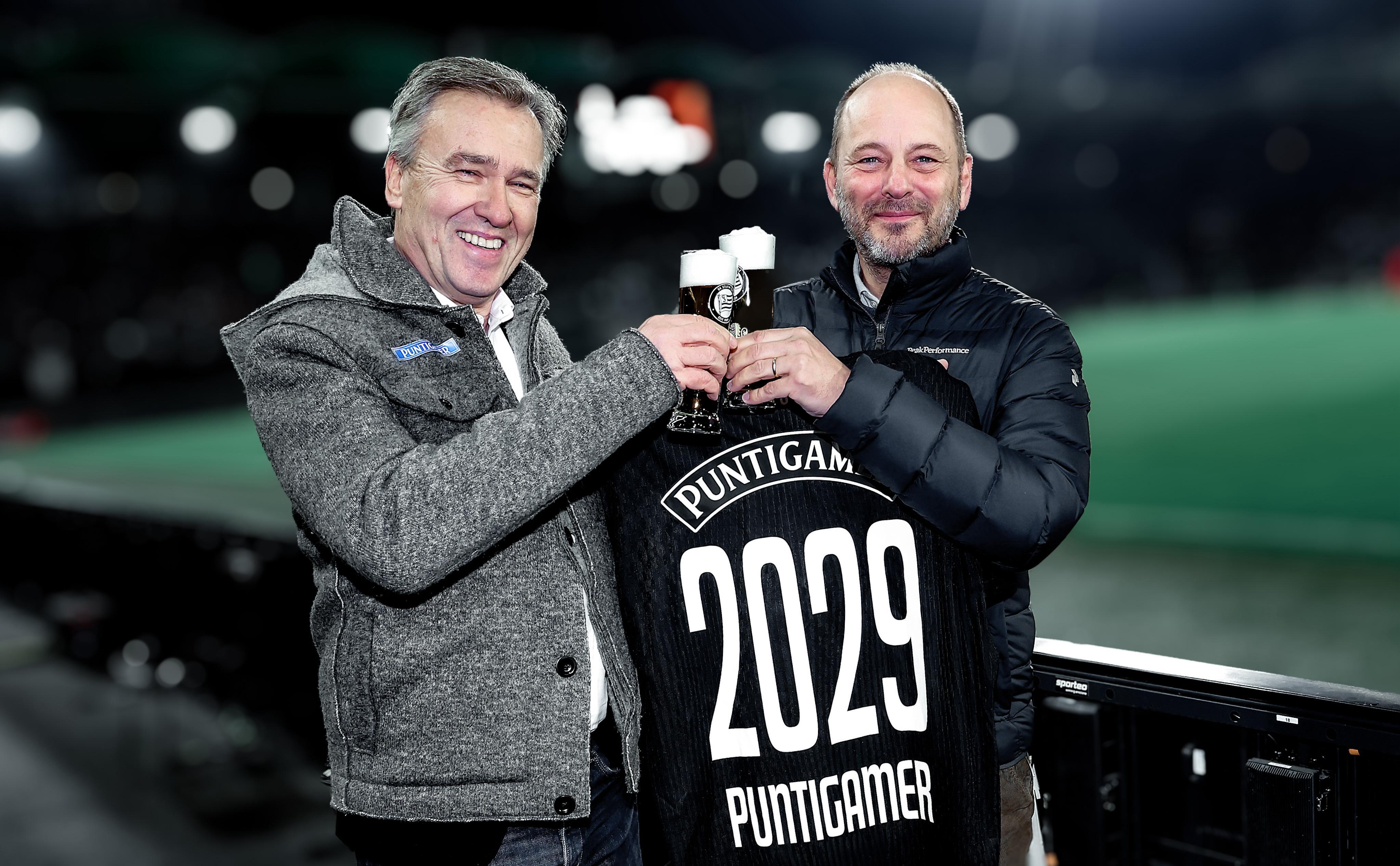 Zwei Männer halten freudig ein Trikot mit Aufdruck "Puntigamer 2029" hoch