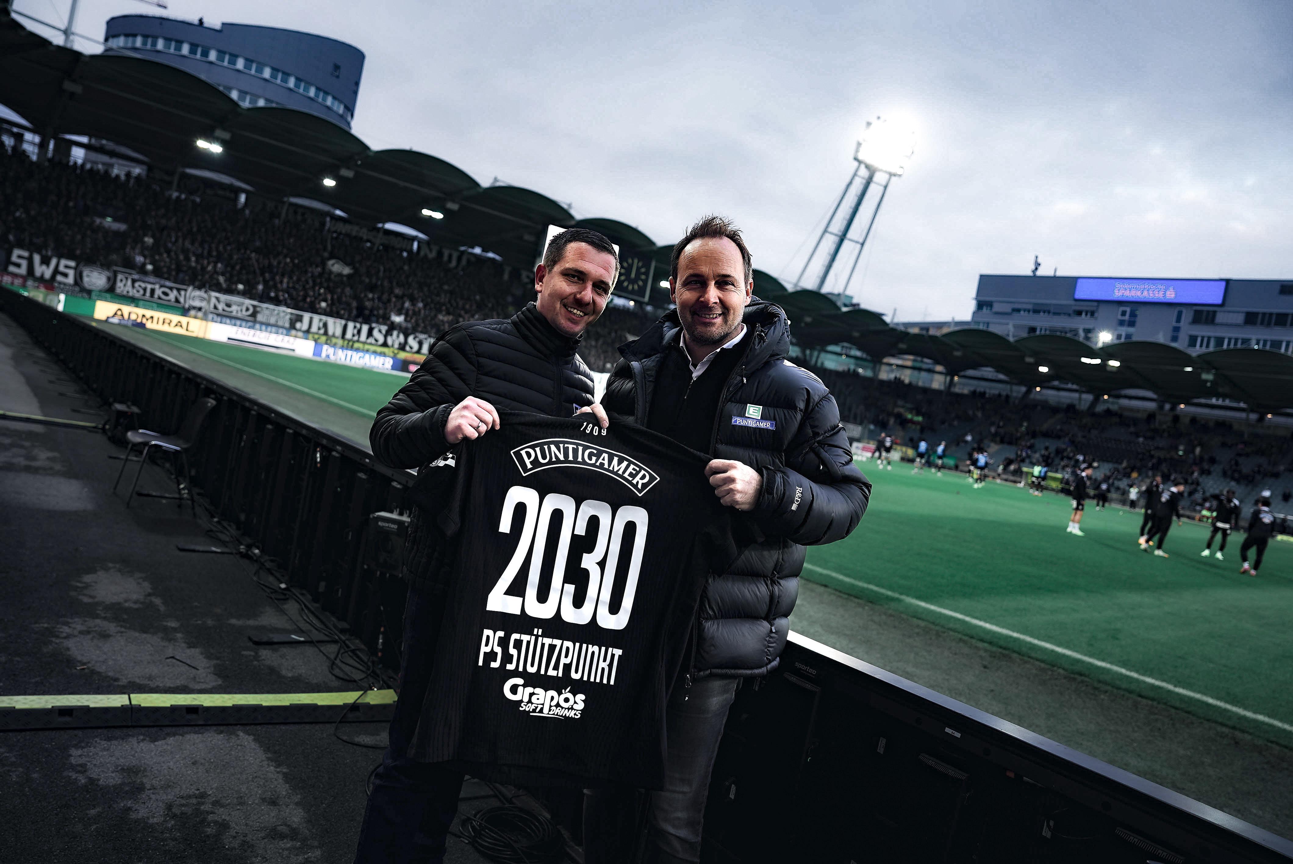 Zwei Männer halten ein schwarzes Trikot hoch