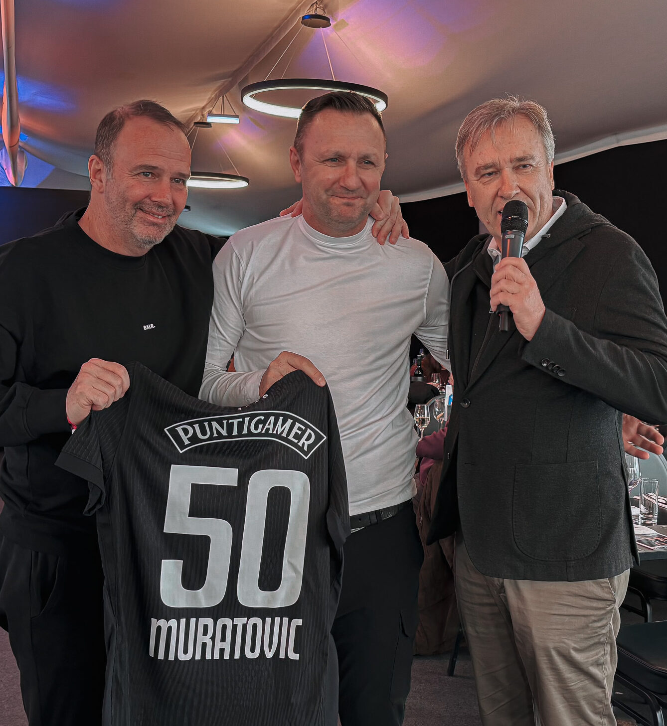 Drei Männer halten ein Trikot