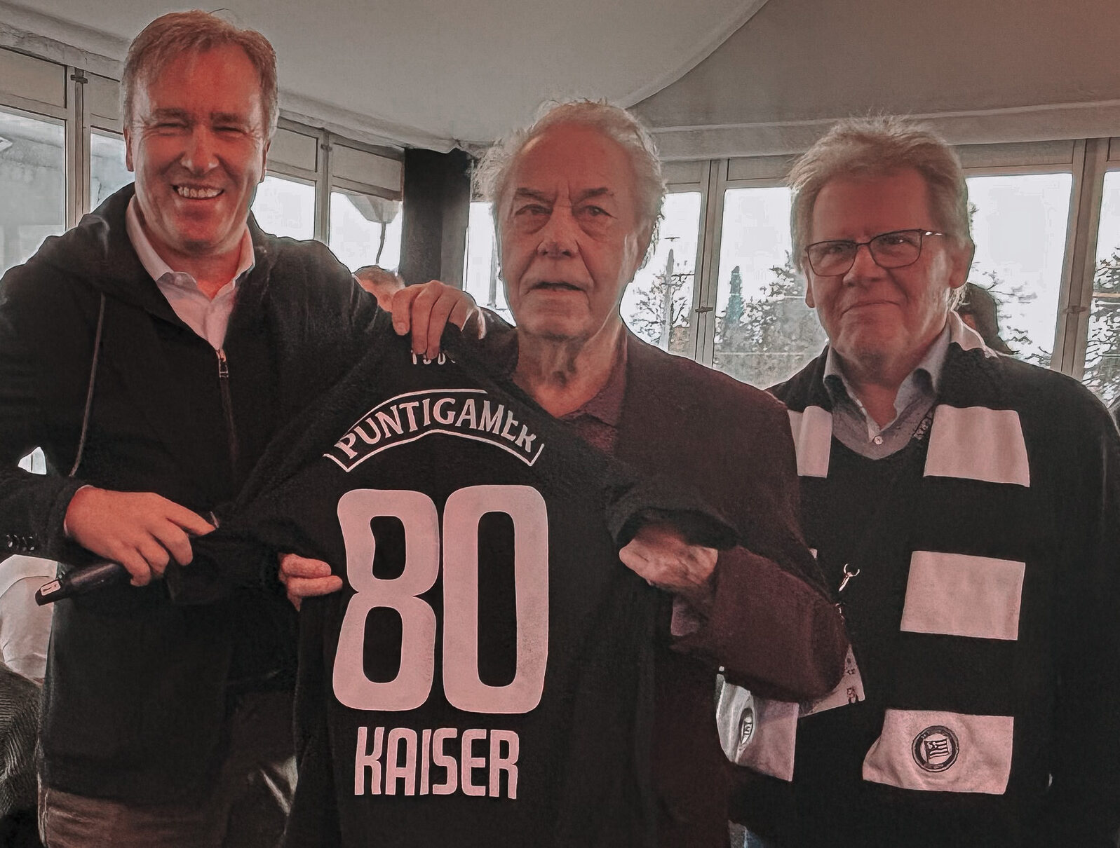 Drei Männer mit einem Trikot in der Hand.