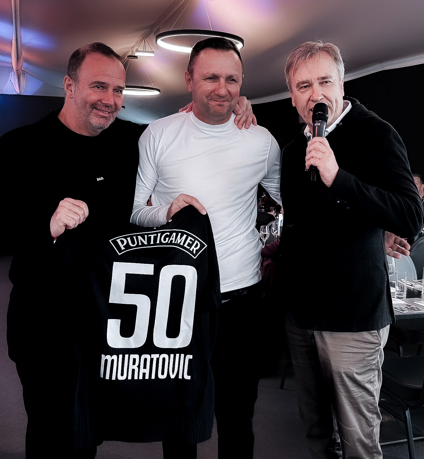 Drei Männer halten ein schwarzes Trikot