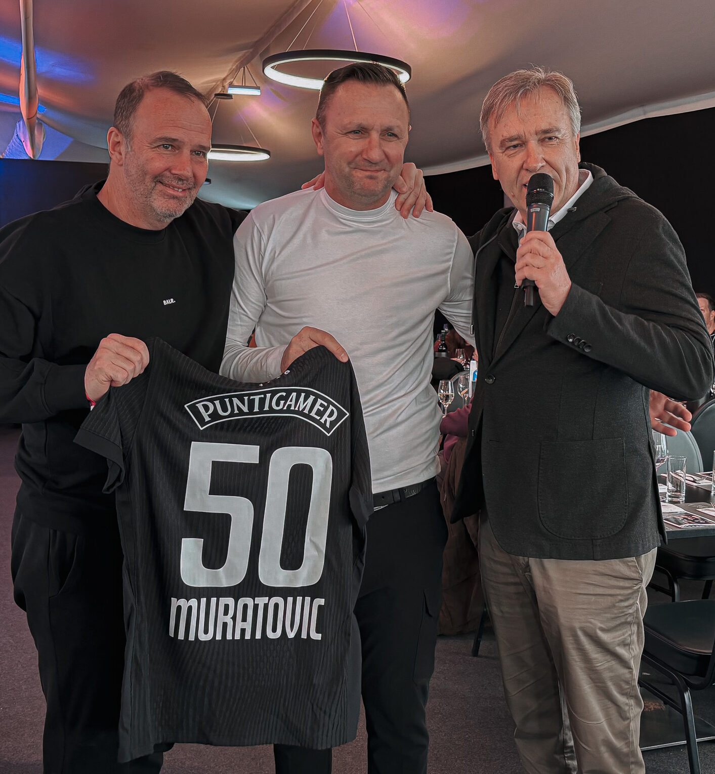 Drei Männer halten ein Trikot.