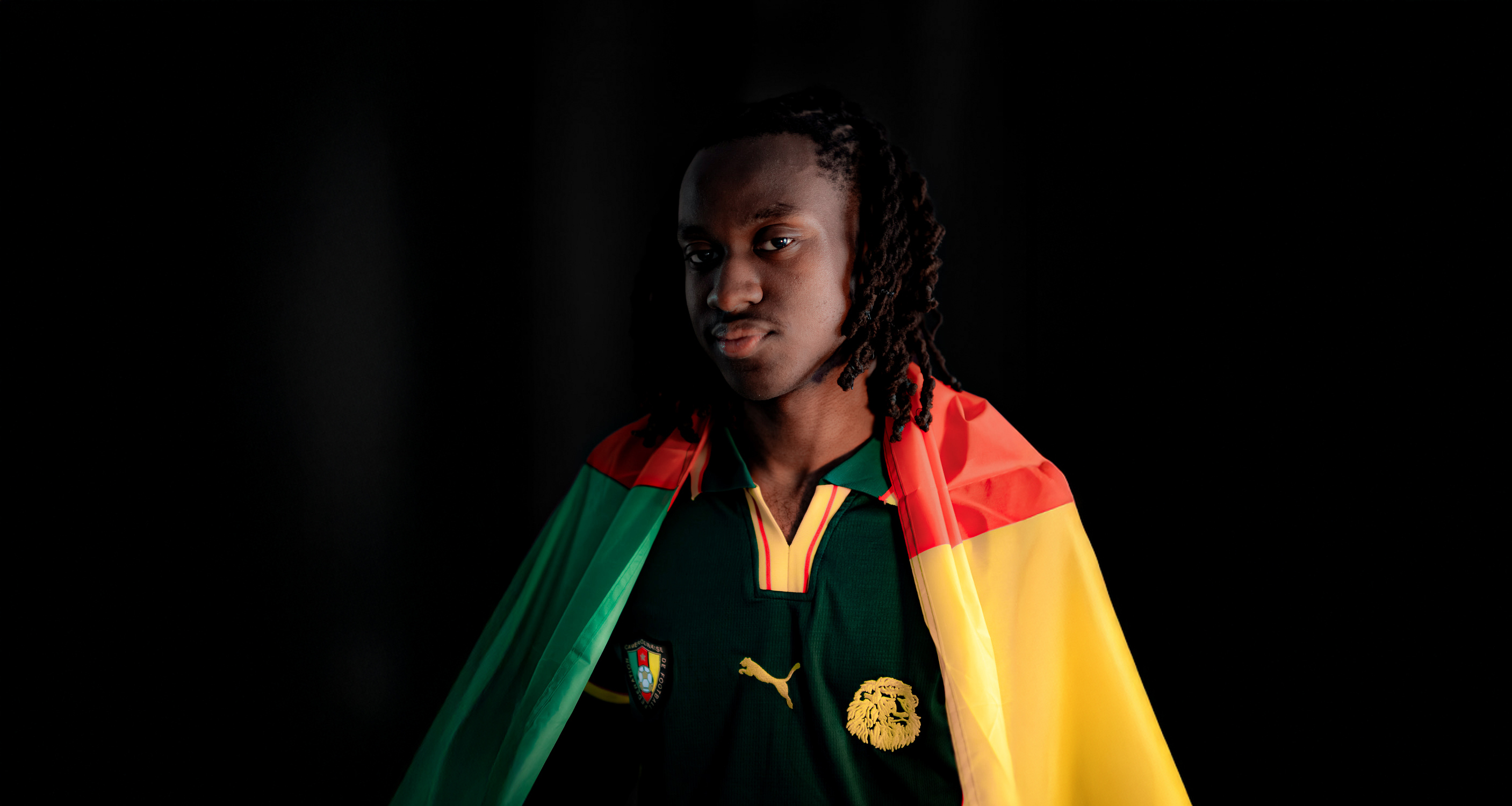 Ein Mann steht mit Kamerun Flagge vor einer dunklen Wand