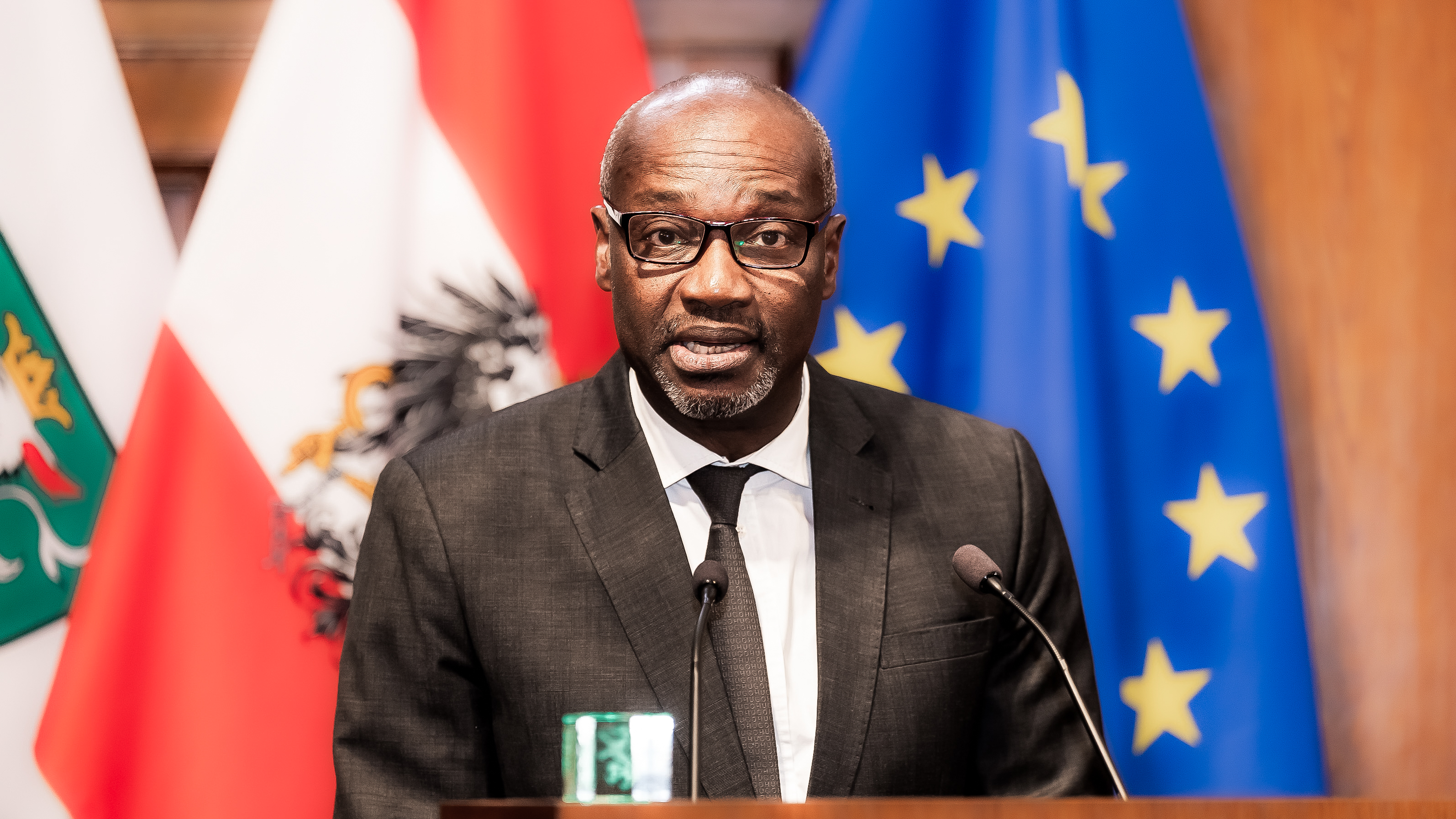 Ein Mann steht im Anzug vor einem Pult mit zwei Mikrofonen