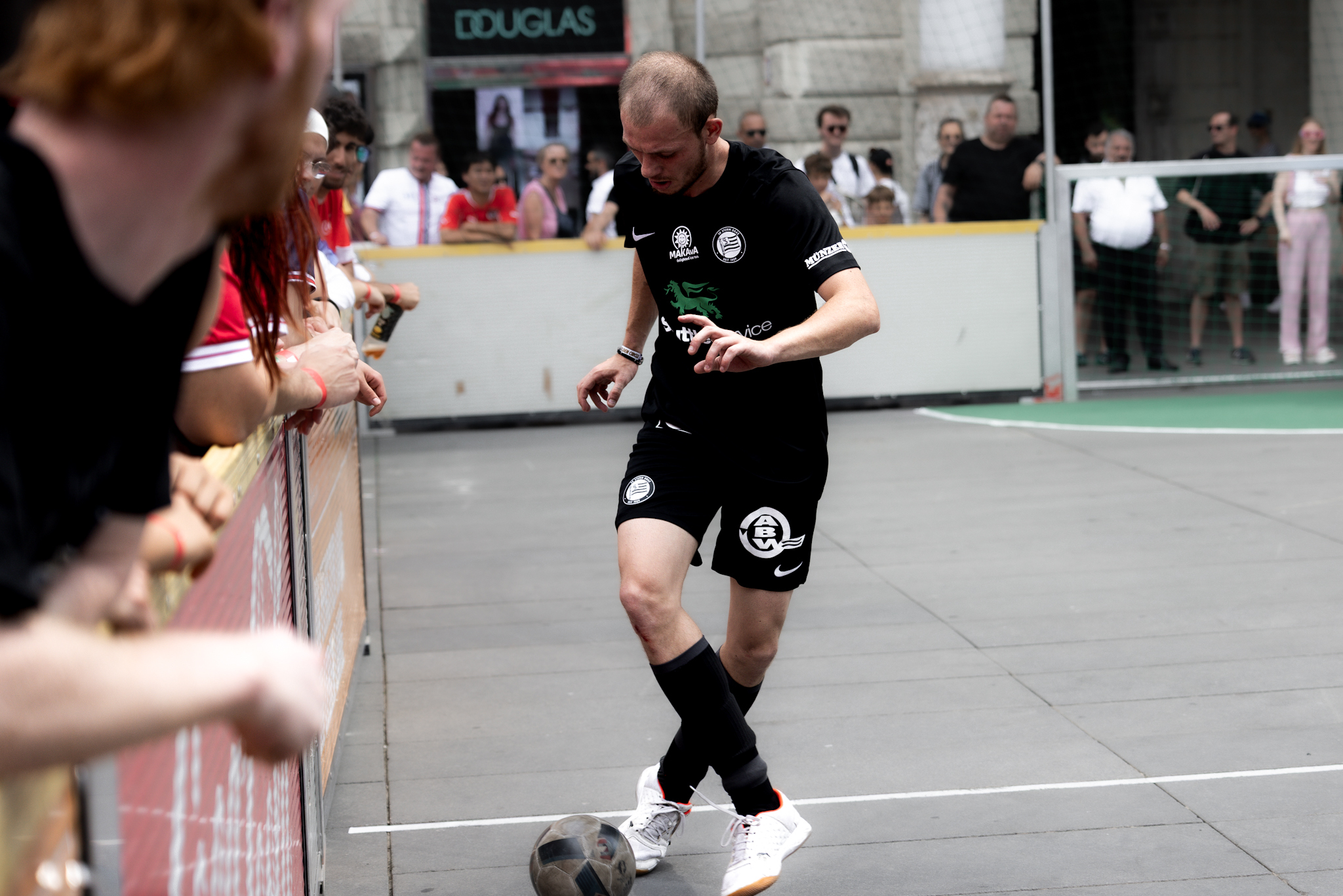 Ein Spieler in schwarzer Hose und Trikot führt einen Ball, viele Leute runderhum sehen zu.