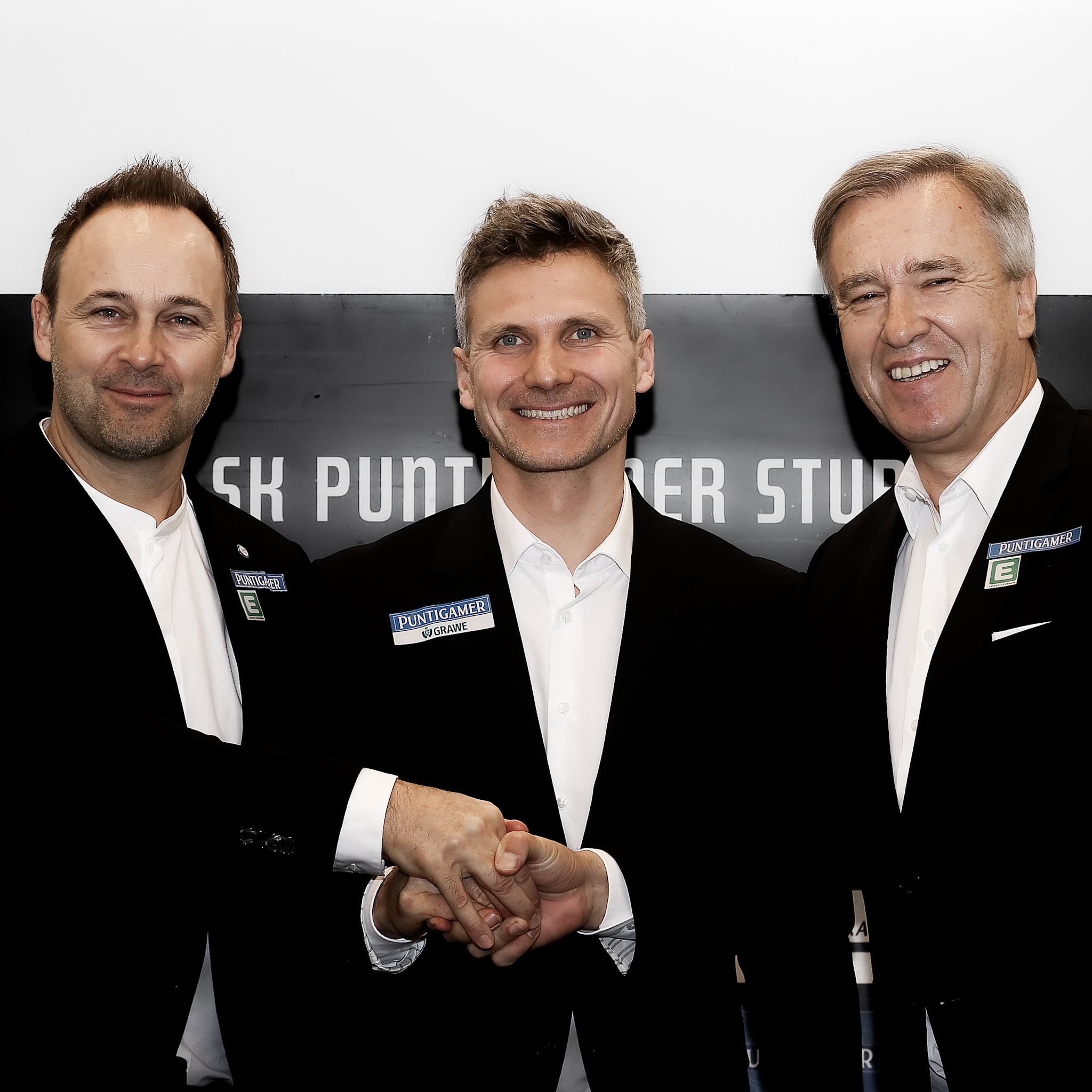Drei Männer im Anzug geben sich die Hand.