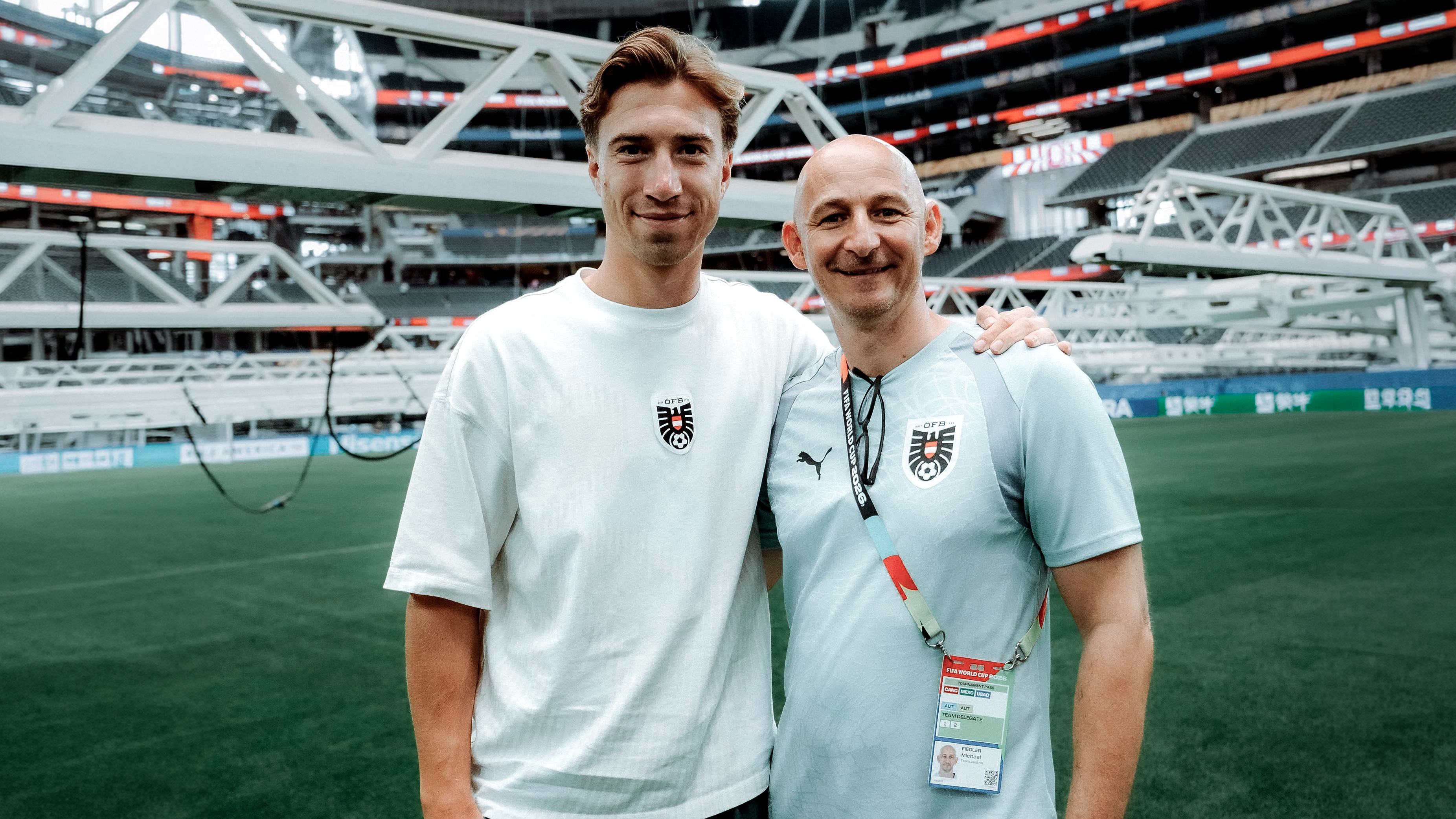 Zwei Männer in weißen Shirts stehen in einem Stadion und umarmen sich