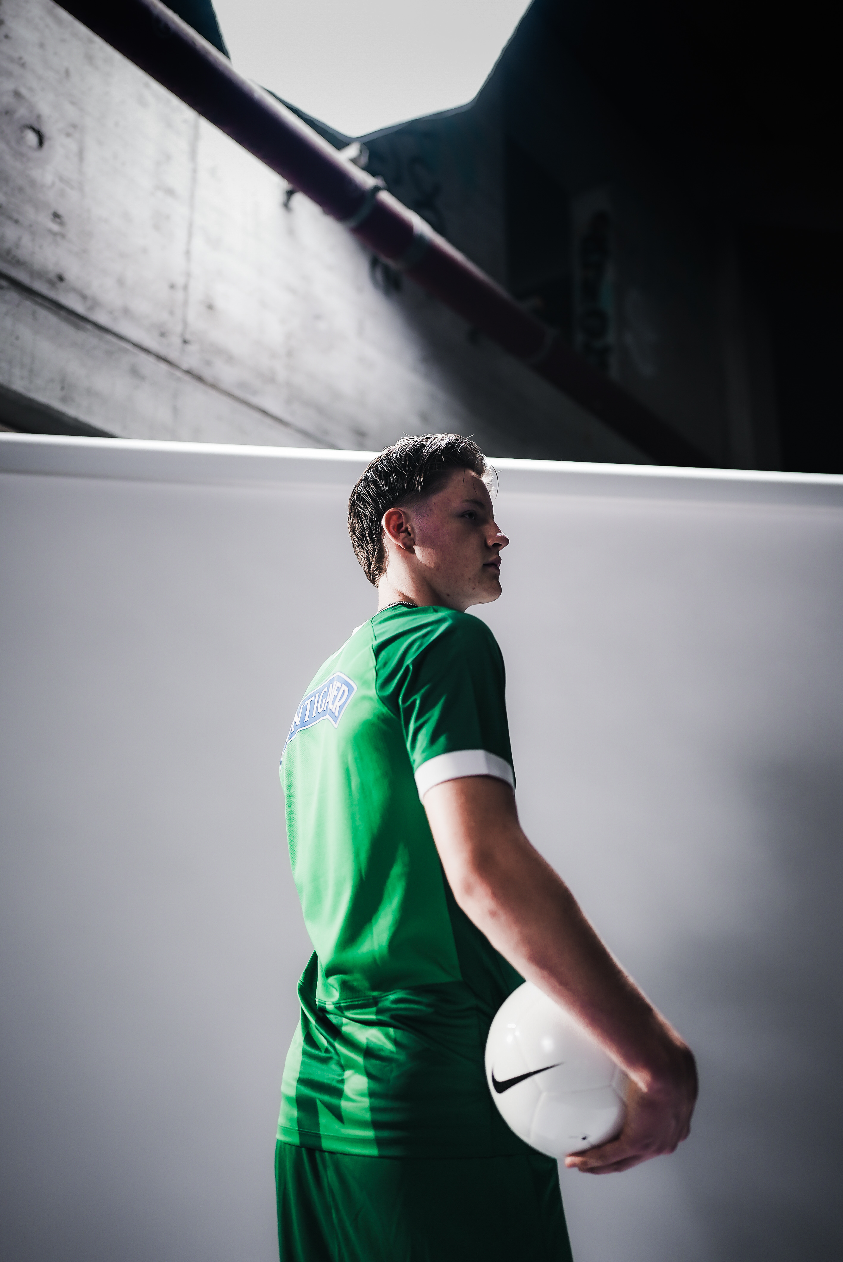 Ein Mann steht mit dem Rücken zur Kamera und hält in einem grünen Trikot einen Ball.