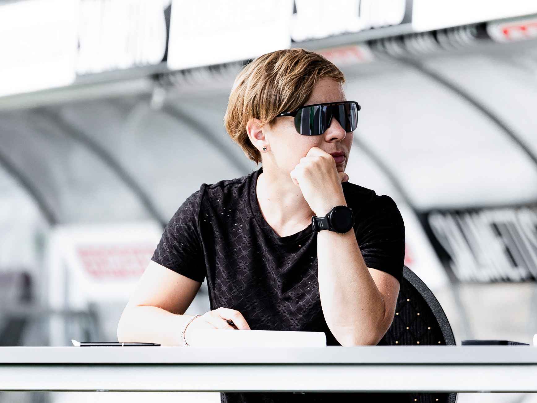 Eine Frau mit Sonnenbrille sitzt an einem Tisch und schaut in eine Richtung