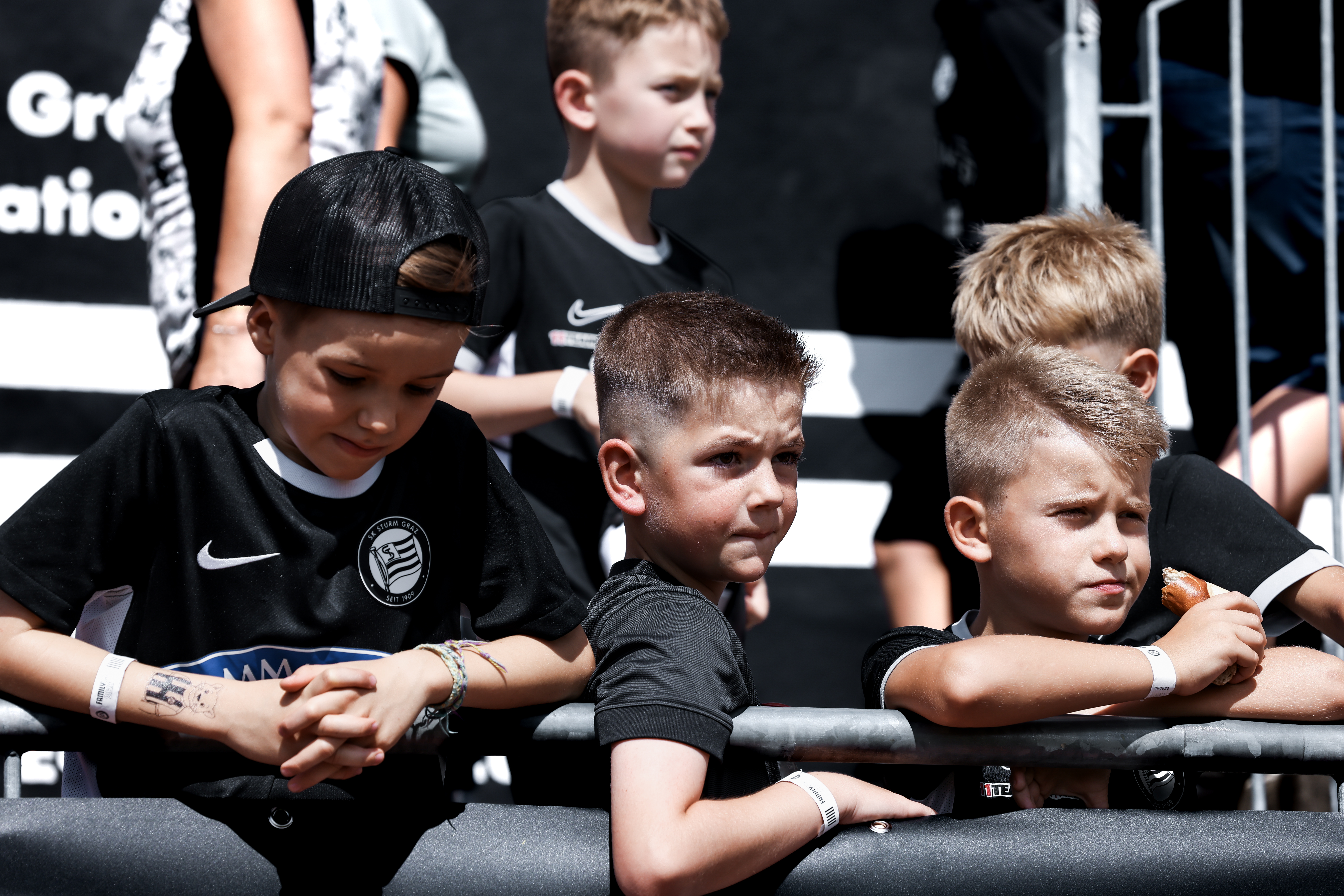 Drei Kinder in einem schwarzen Trikot lehnen an einem Geländer und lachen