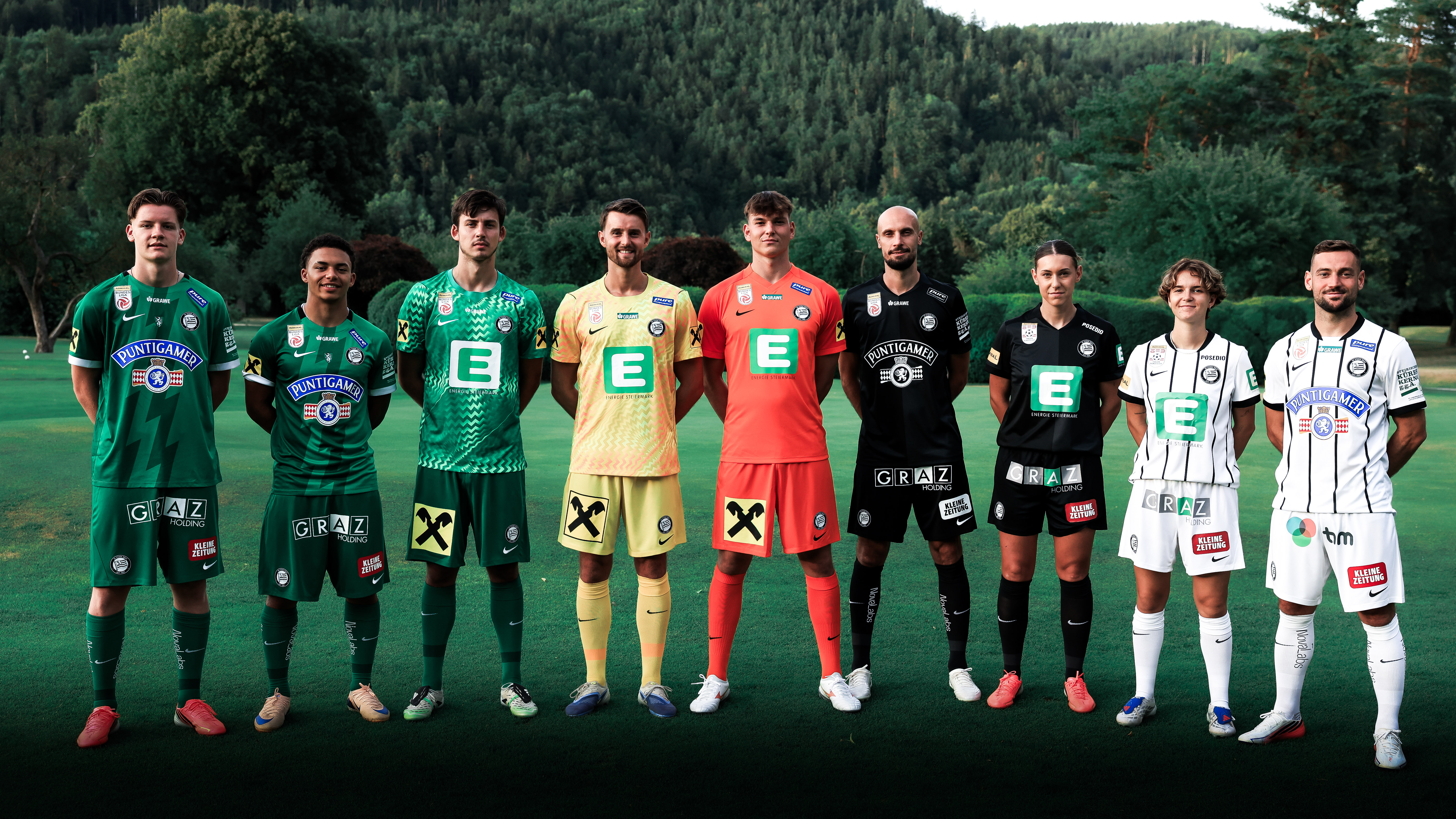 Sieben Männer und zwei Frauen stehen in Fußballshirts mit verschränkten Armen da und schauen in die Kamera.