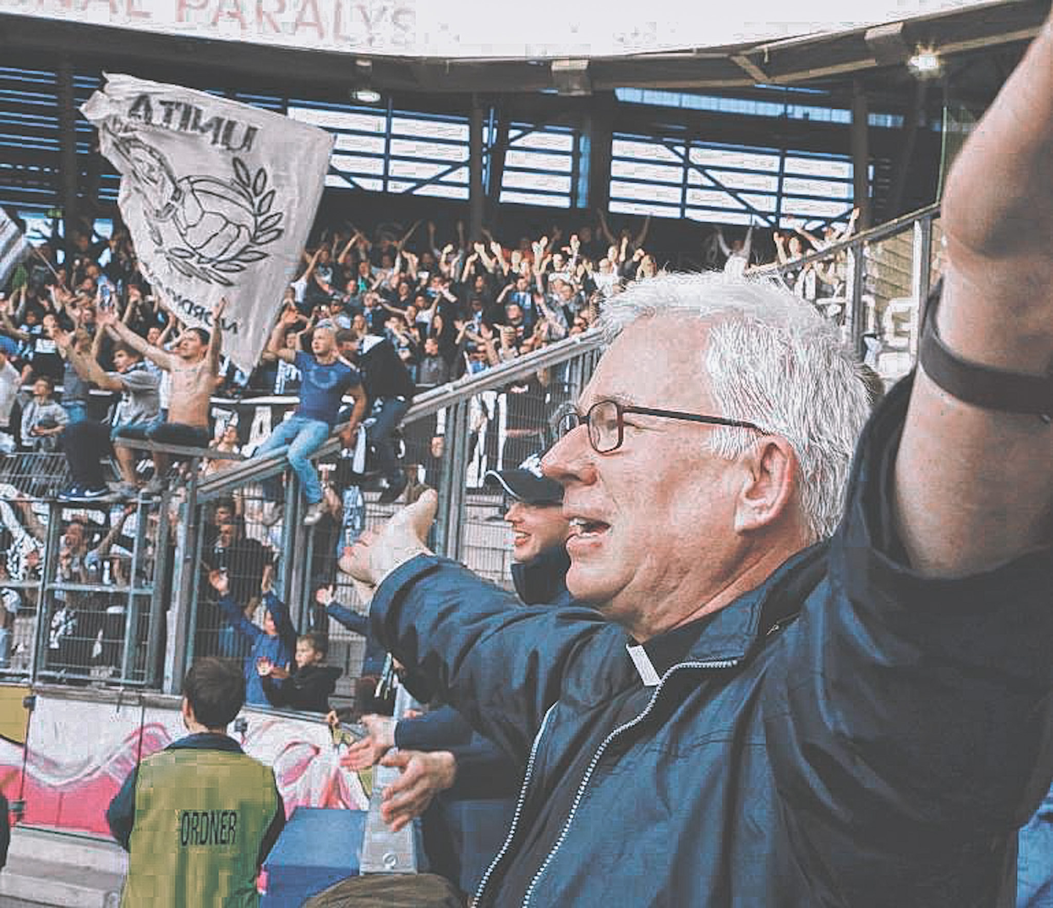 Priester jubelt mit ausgebreiteten Armen in einem Fußballstadion.