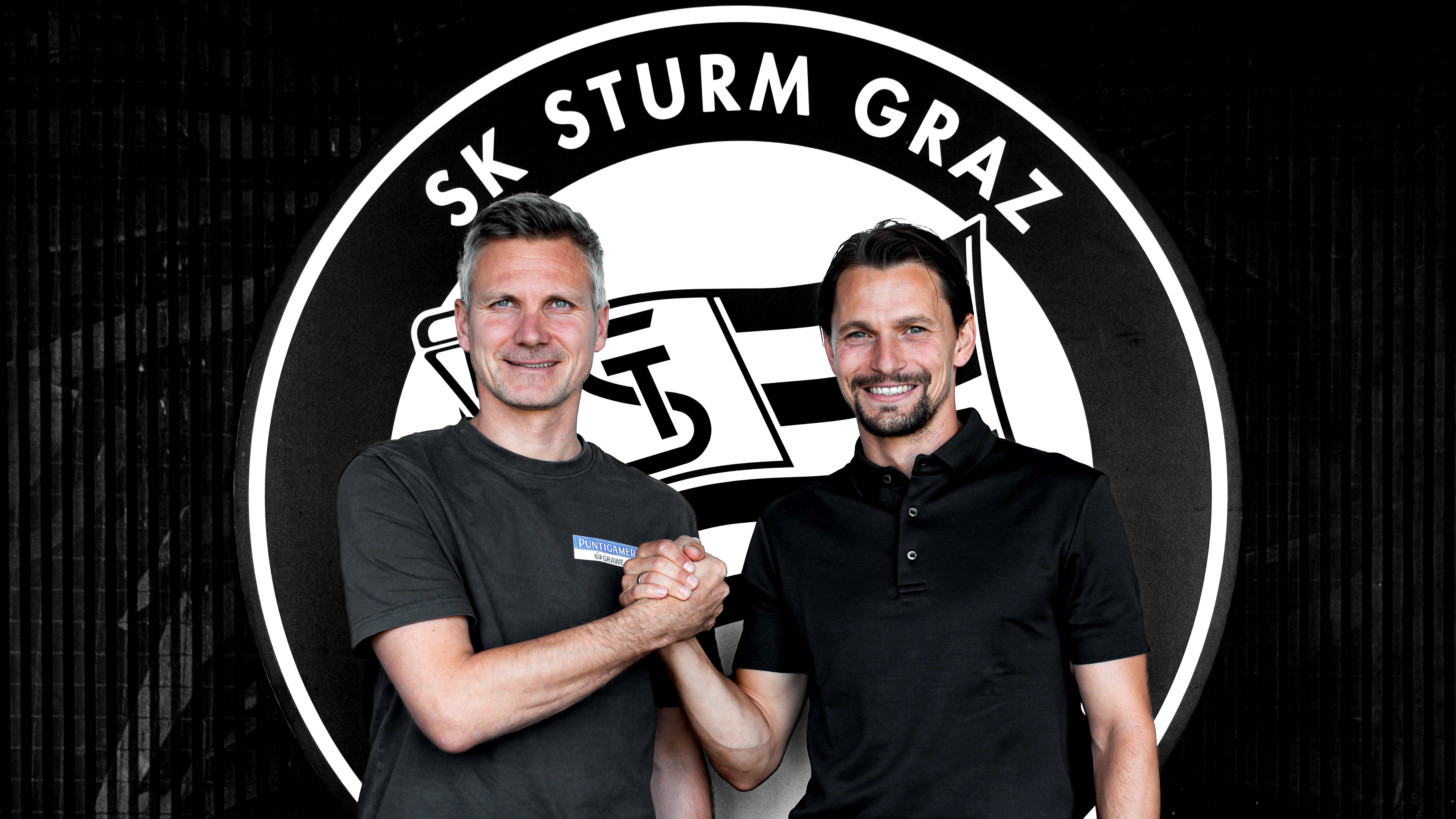 Zwei Männer in einem dunklen Shirt geben sich vor einem schwarz-weißen Logo die Hände