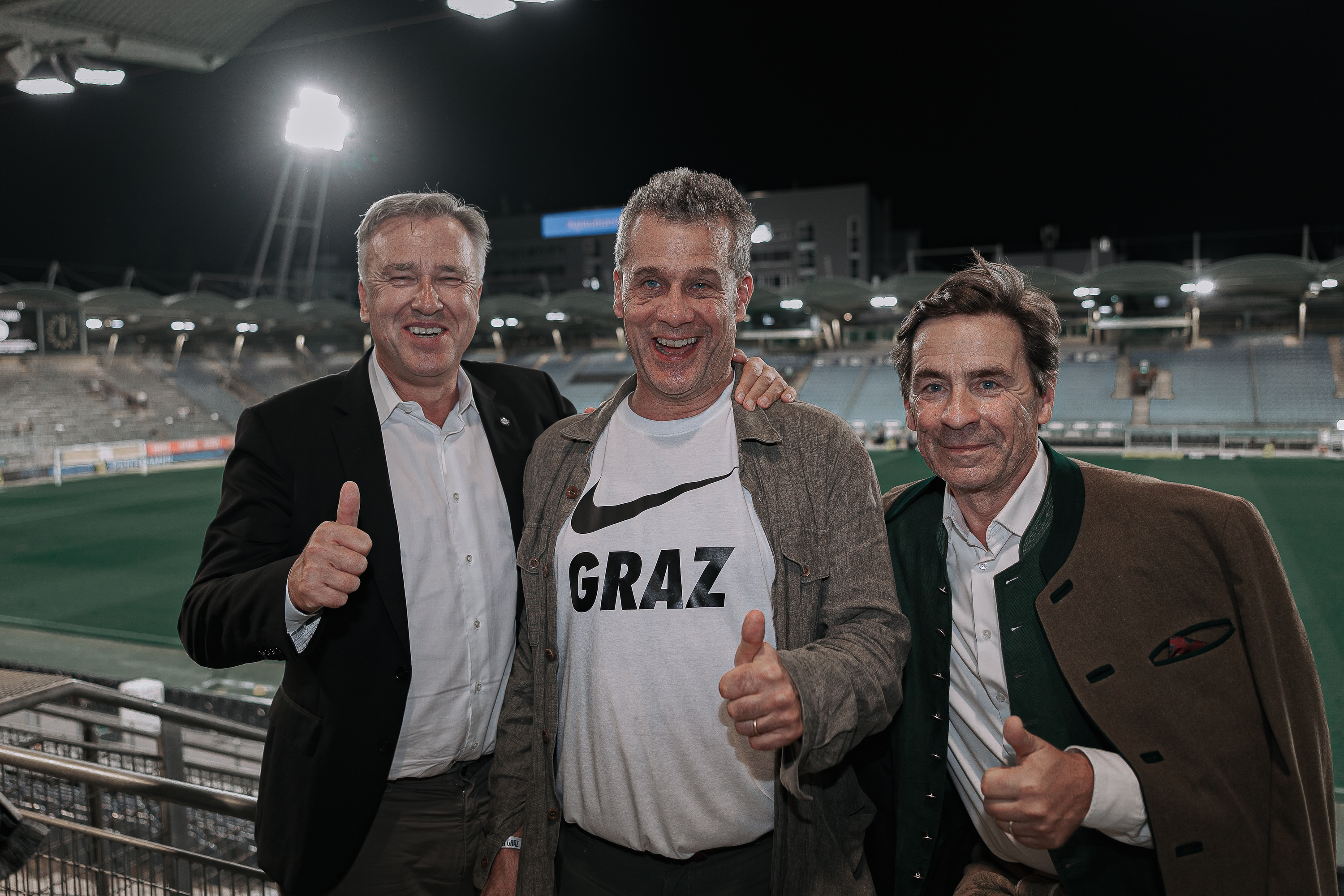 Drei Männer posieren im Stadion.