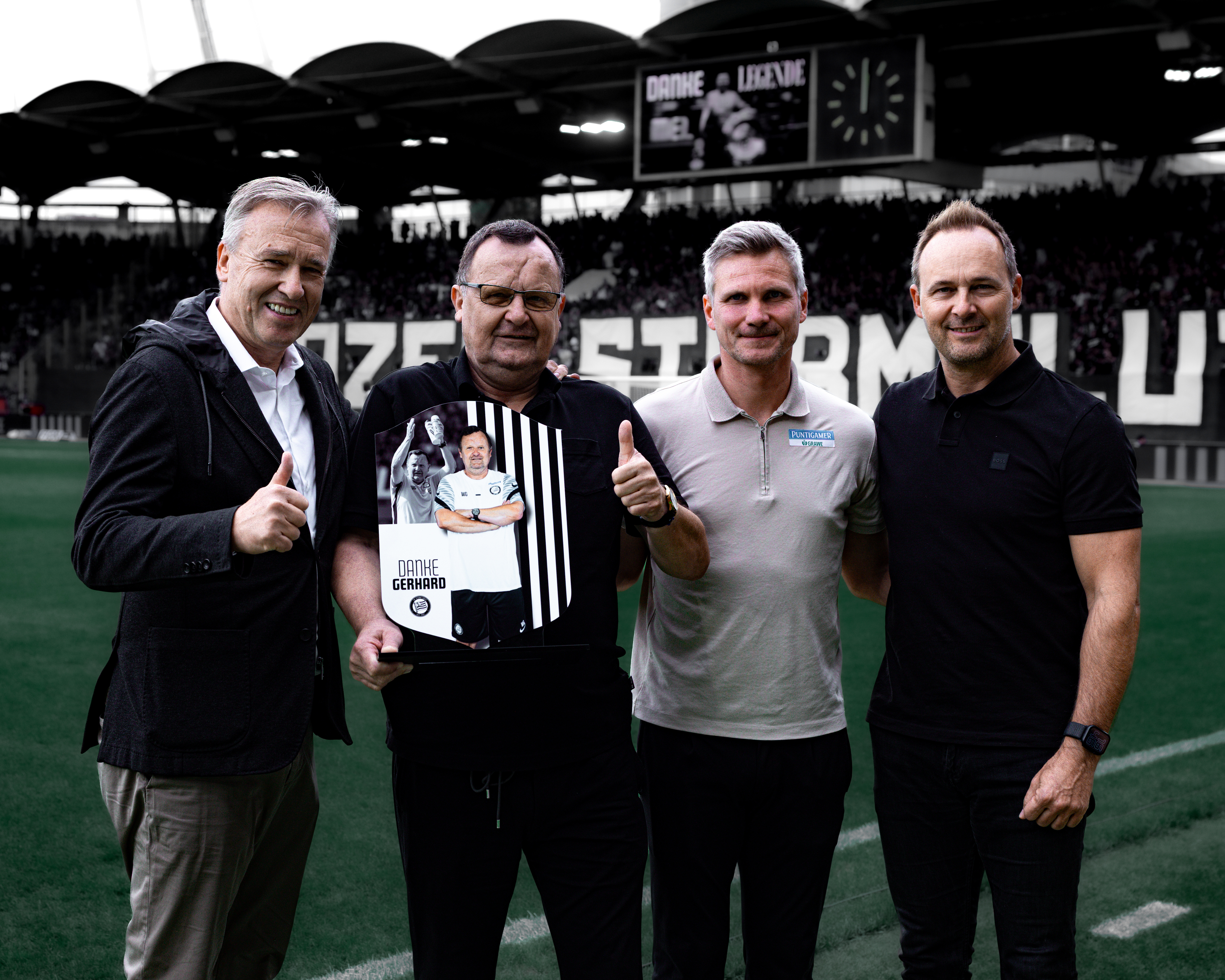 Vier Personen stehen in einem Stadion und übergeben eine Trophäe