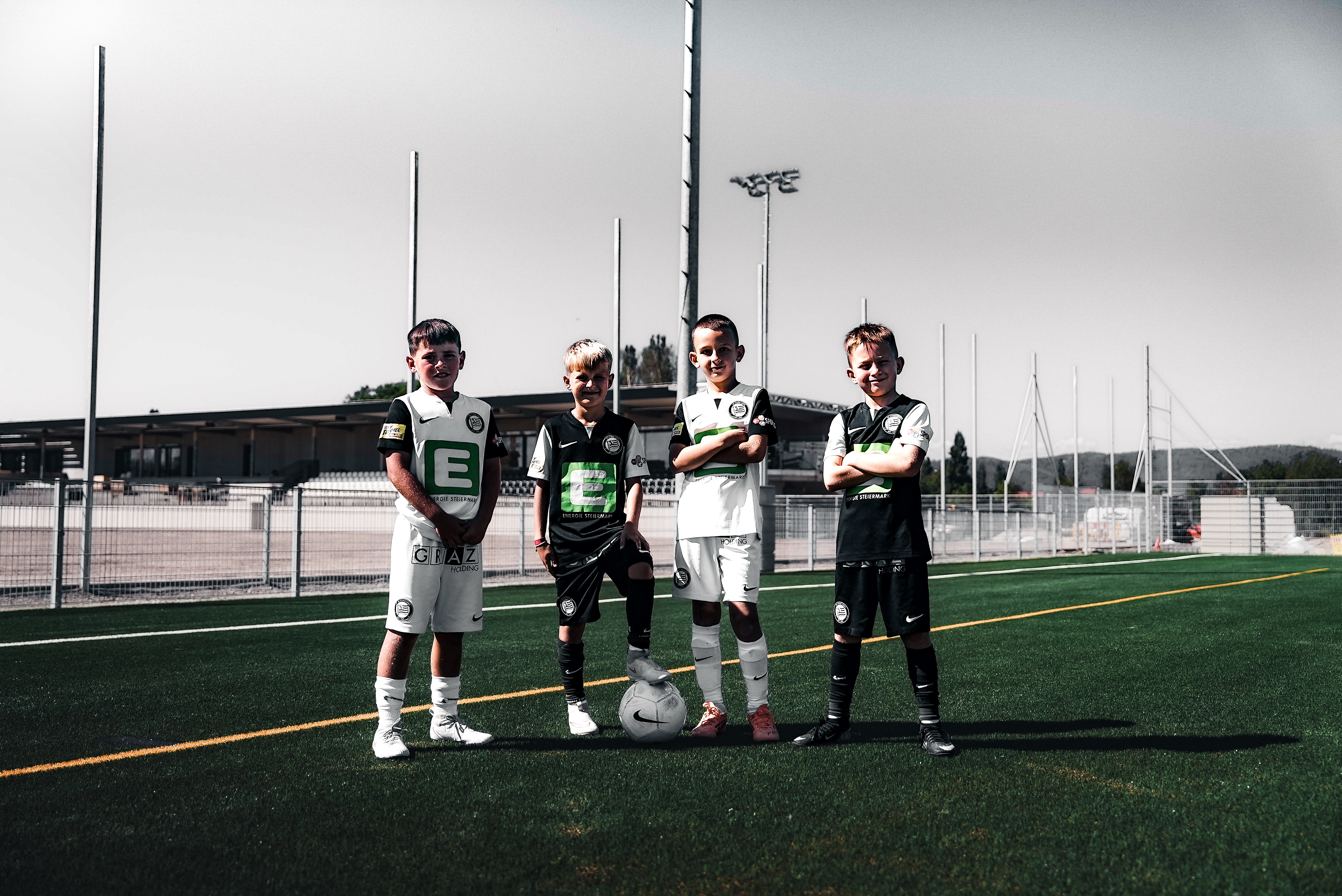 Vier Jungs mit Trikot und einem Ball auf einem Fußballfeld.