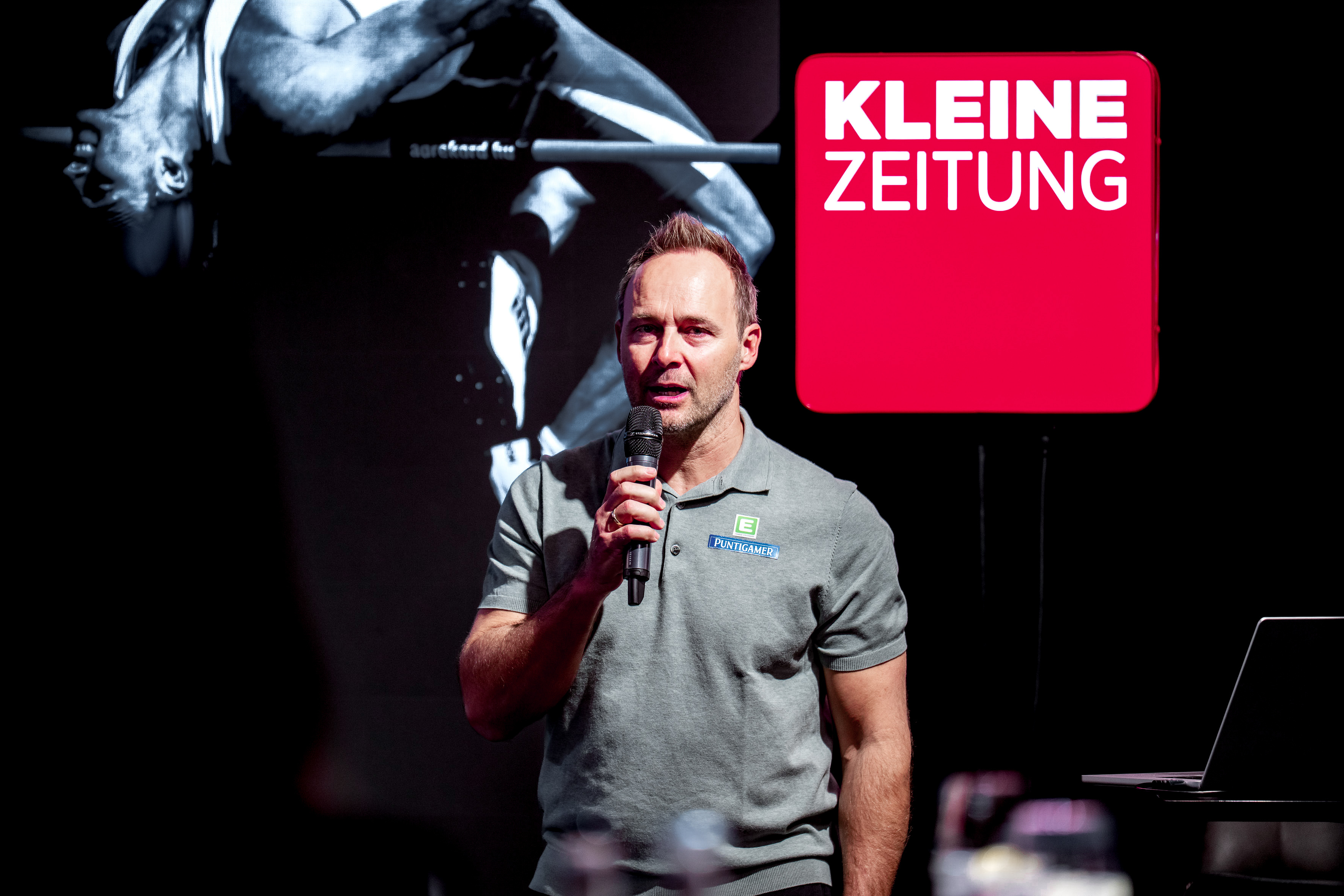 Ein Mann steht mit einem Mikrofon vor einer Leinwand.