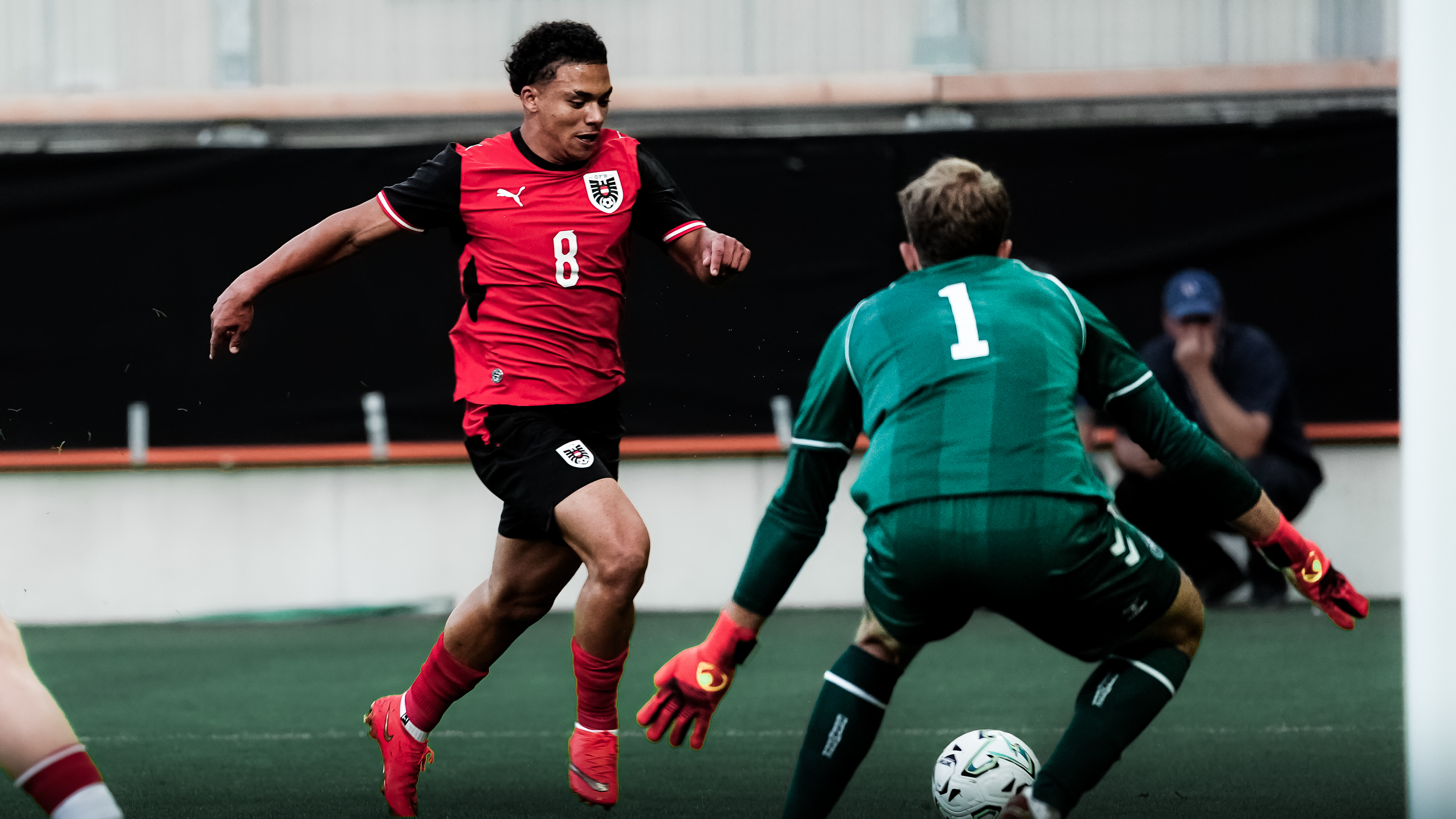 Ein Spieler in einem rot-schwarzen Trikot schießt einen weißen Ball auf einen Torhüter.