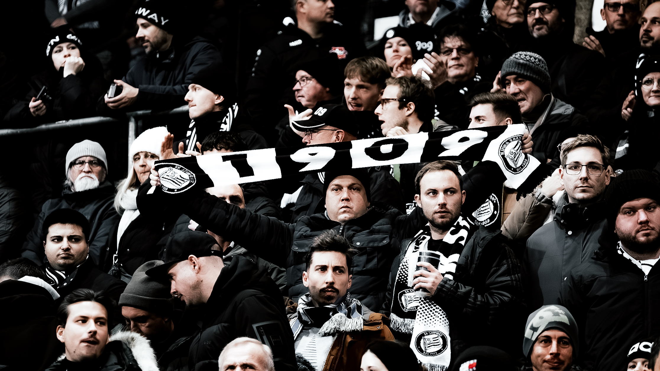 Viele Menschen stehen und ein Mensch hält einen schwarz-weißen Schal in die Höhe