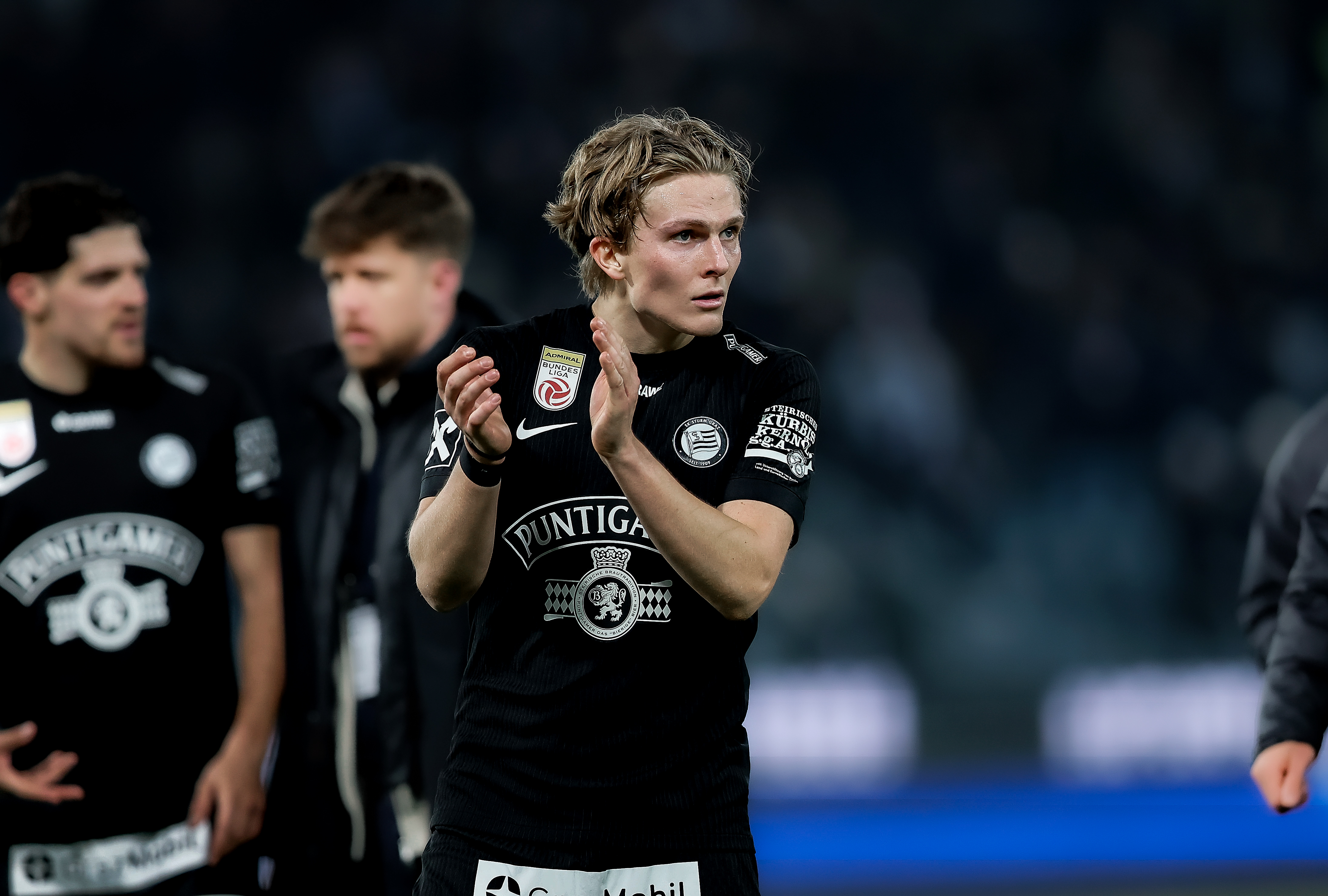 Ein Spieler im Vordergrund im schwarzen Trikot klatscht, im Hintergrund sind 2 weitere, die reden