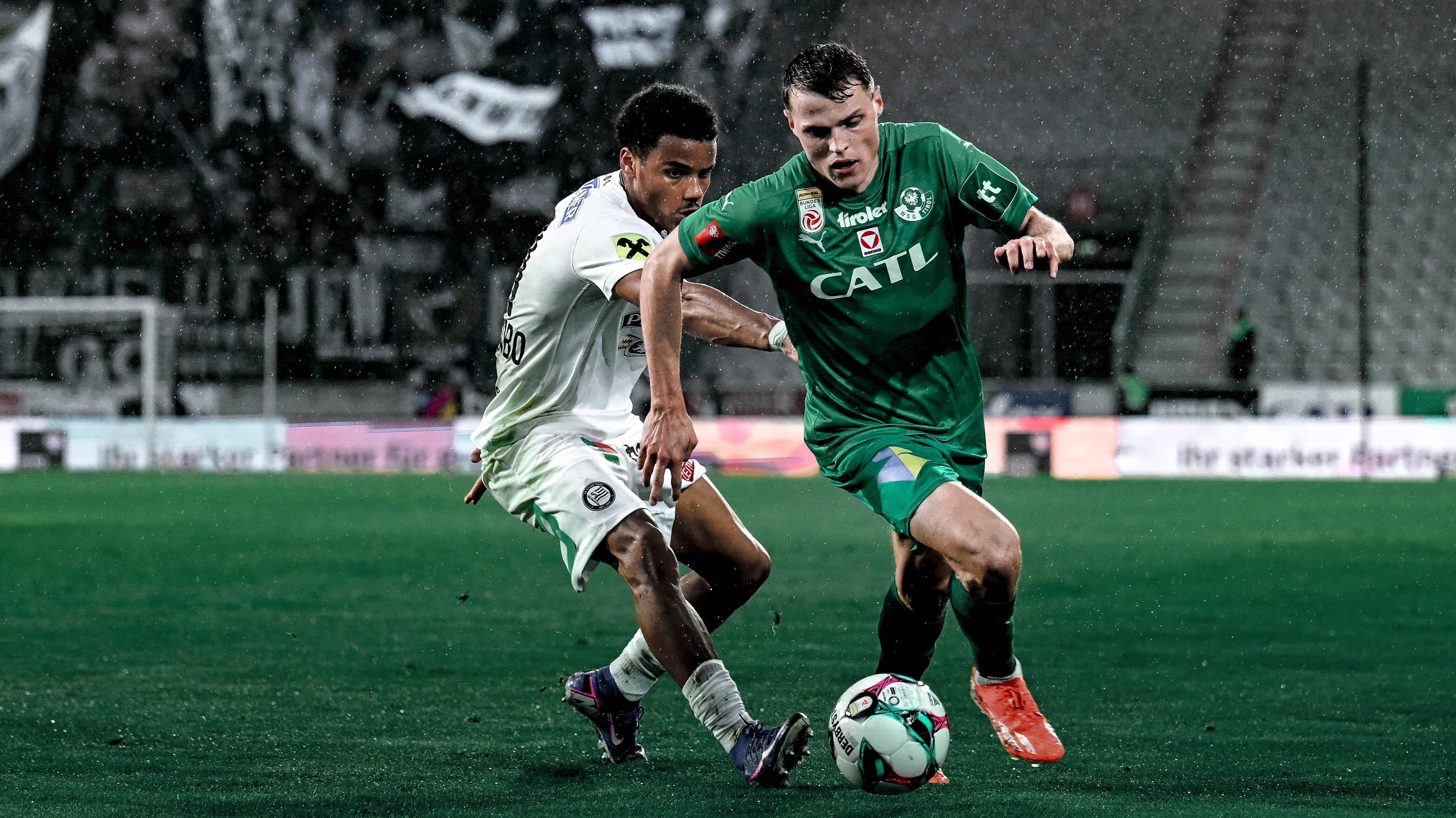 Zwei Spieler, einer in weiß und einer in grün gekleidet, kämpfen um den Ball