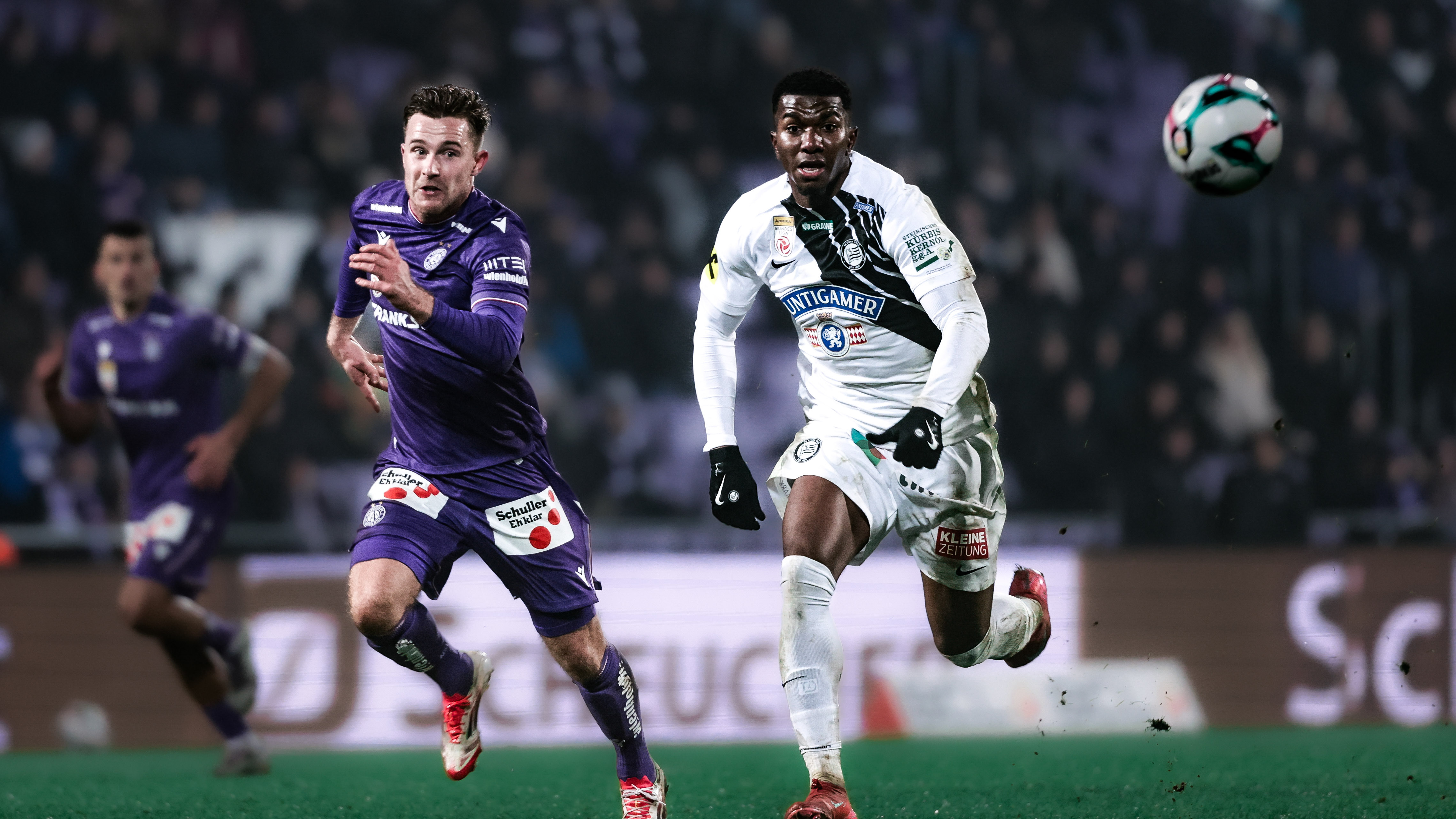 Zwei Spieler in weiß und in violett kämpfen um den Ball