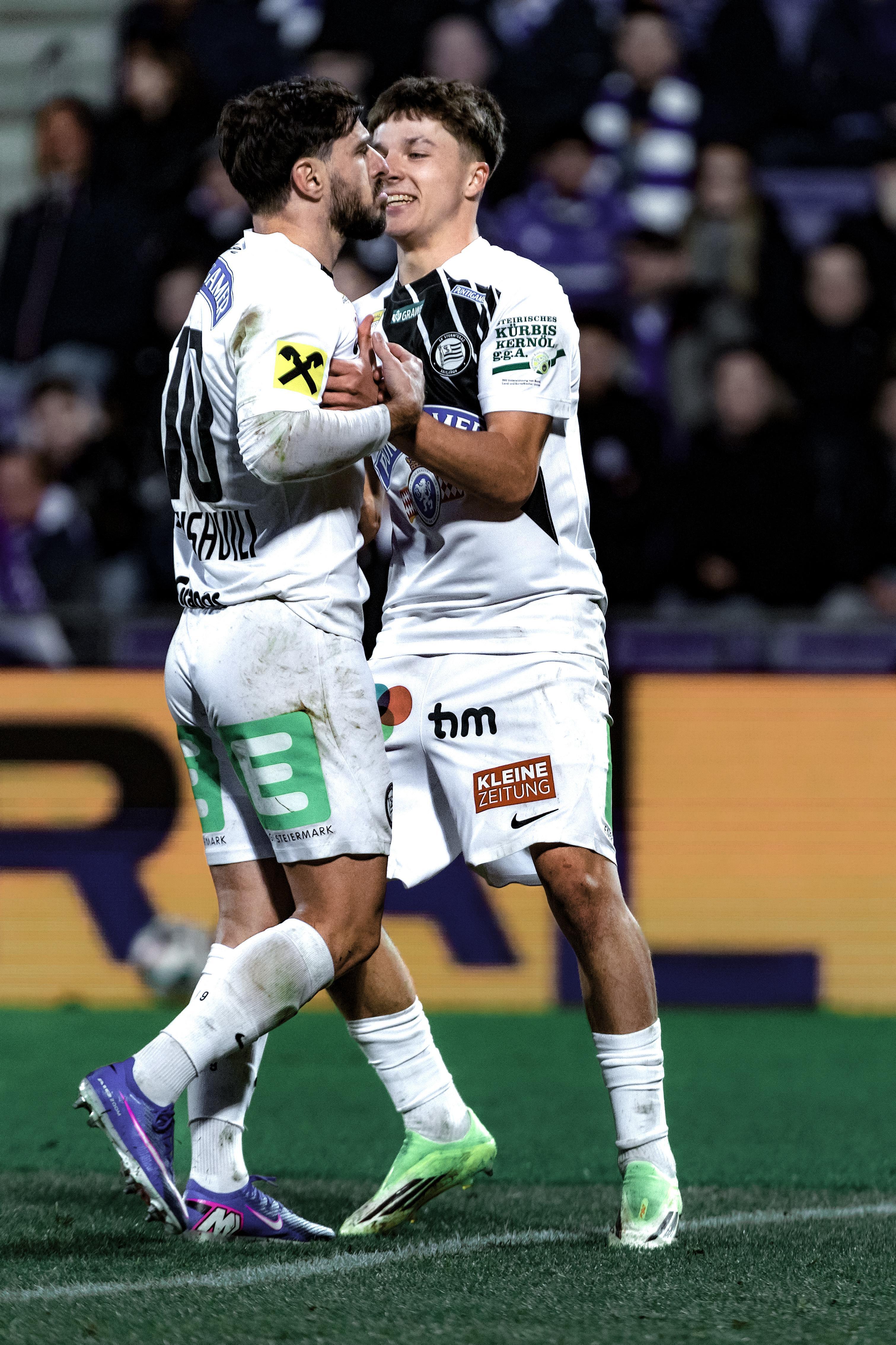 Zwei Spieler in weißen Trikots und Hosen umarmen sich.