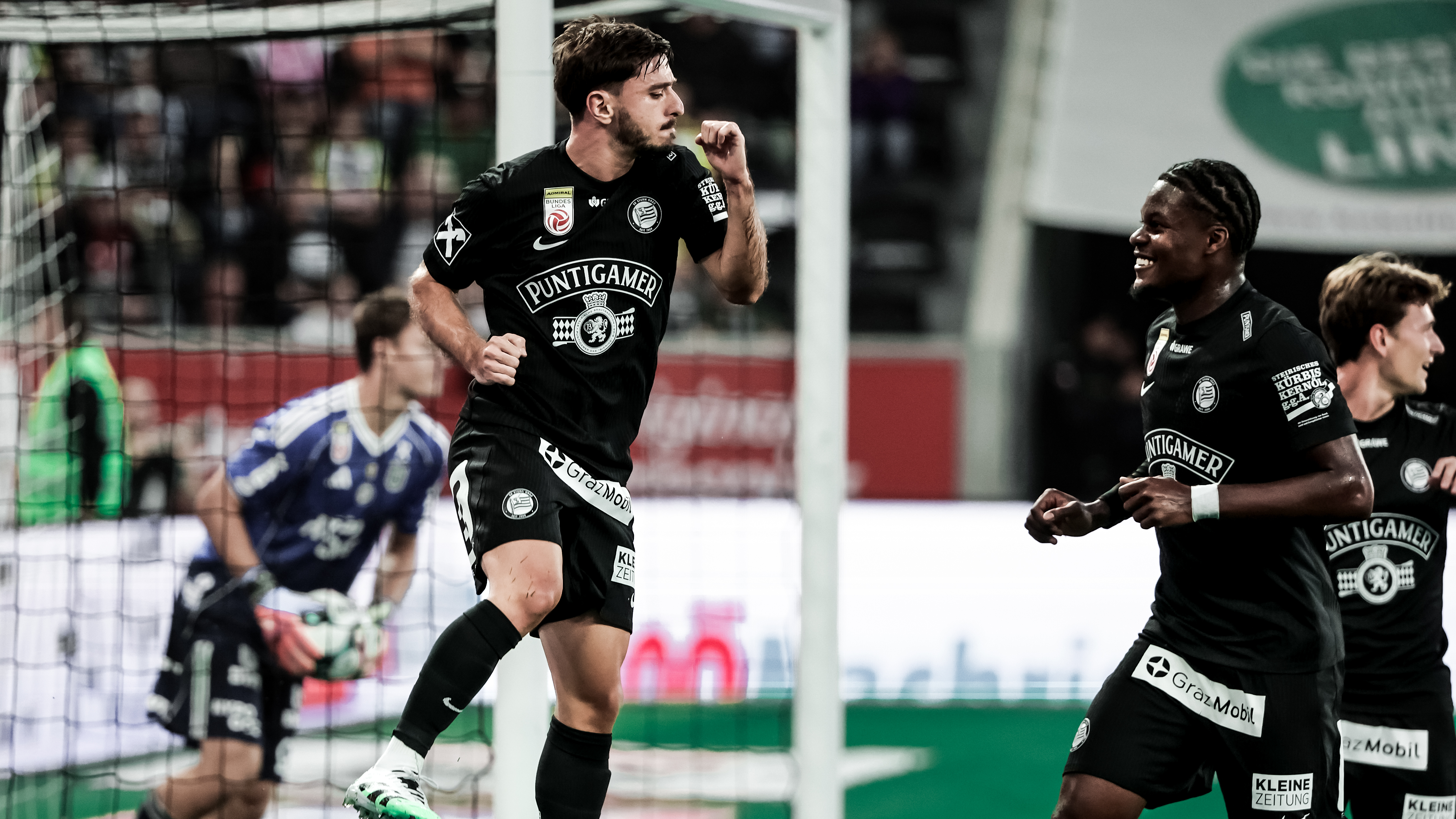 Drei Spieler in schwarzen Trikot jubeln über einen Treffer, im Hintergrund sieht man ein Tor