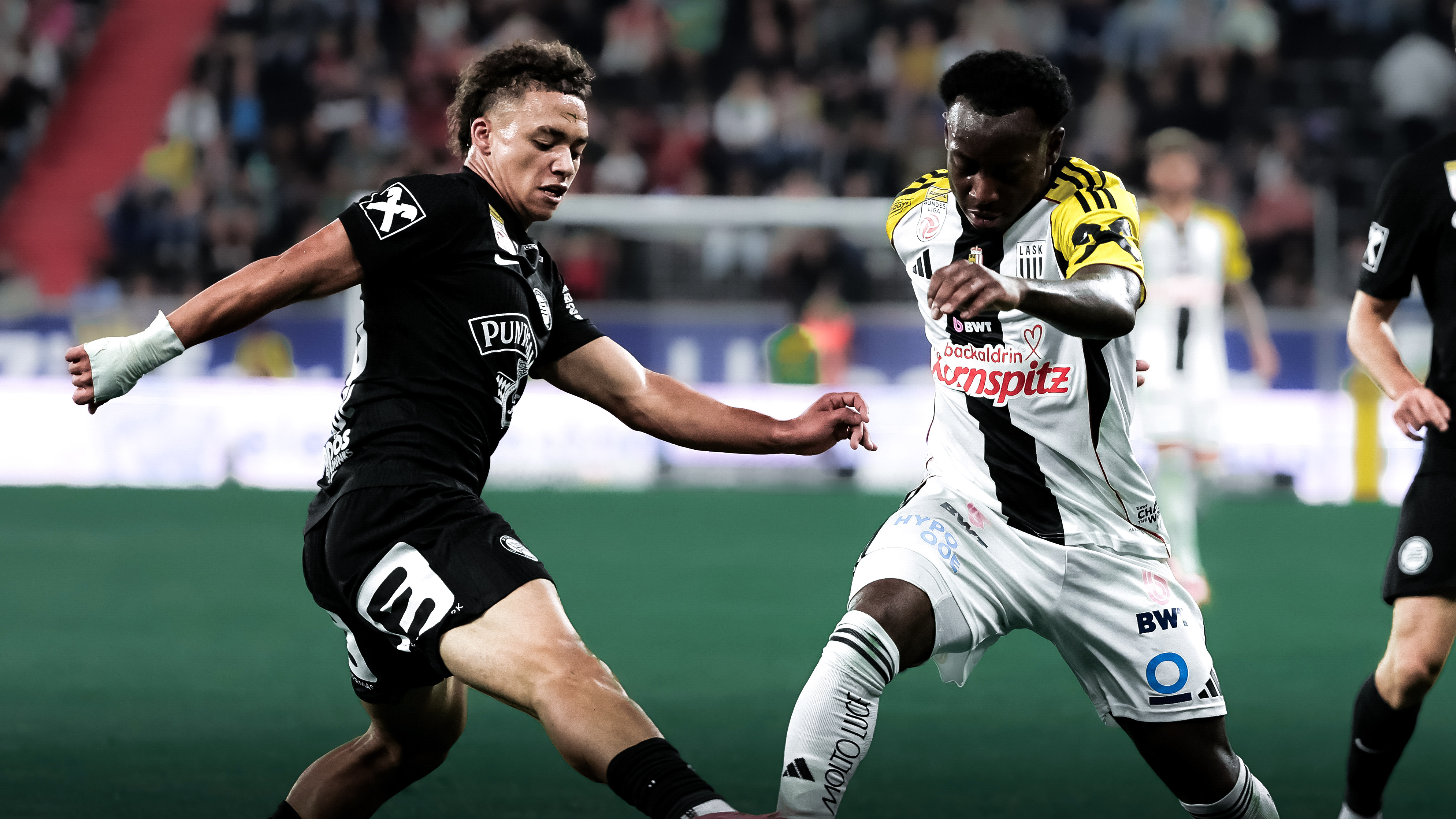 Ein Spieler in einem schwarzen Trikot kämpft gegen einen Spieler in einem schwarz-weißen Trikot um den Ball