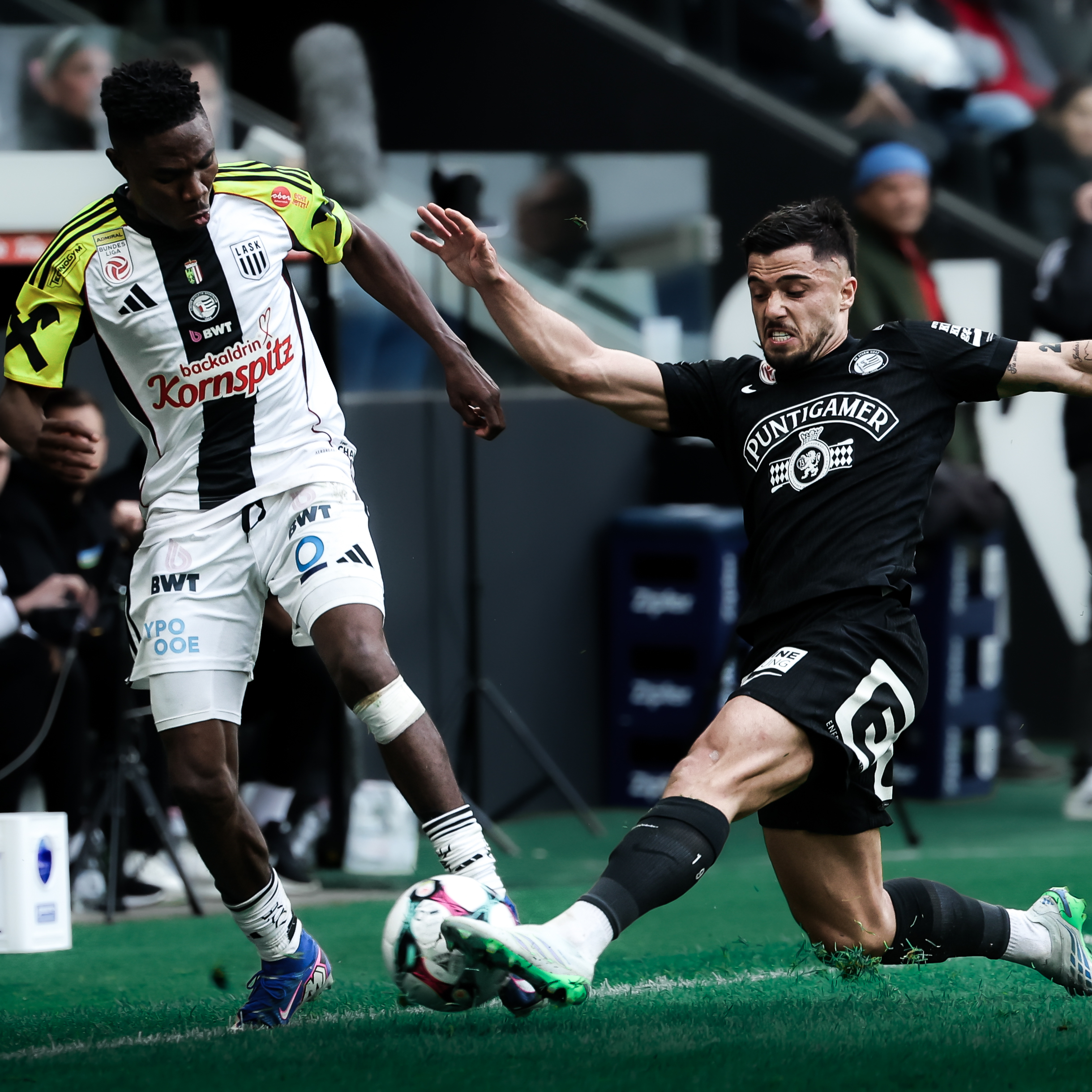 Ein Spieler in einem schwarzen Trikot kämpft mit einem Spieler in einem weiß-schwarz-gelben Trikot um einen weißen Ball