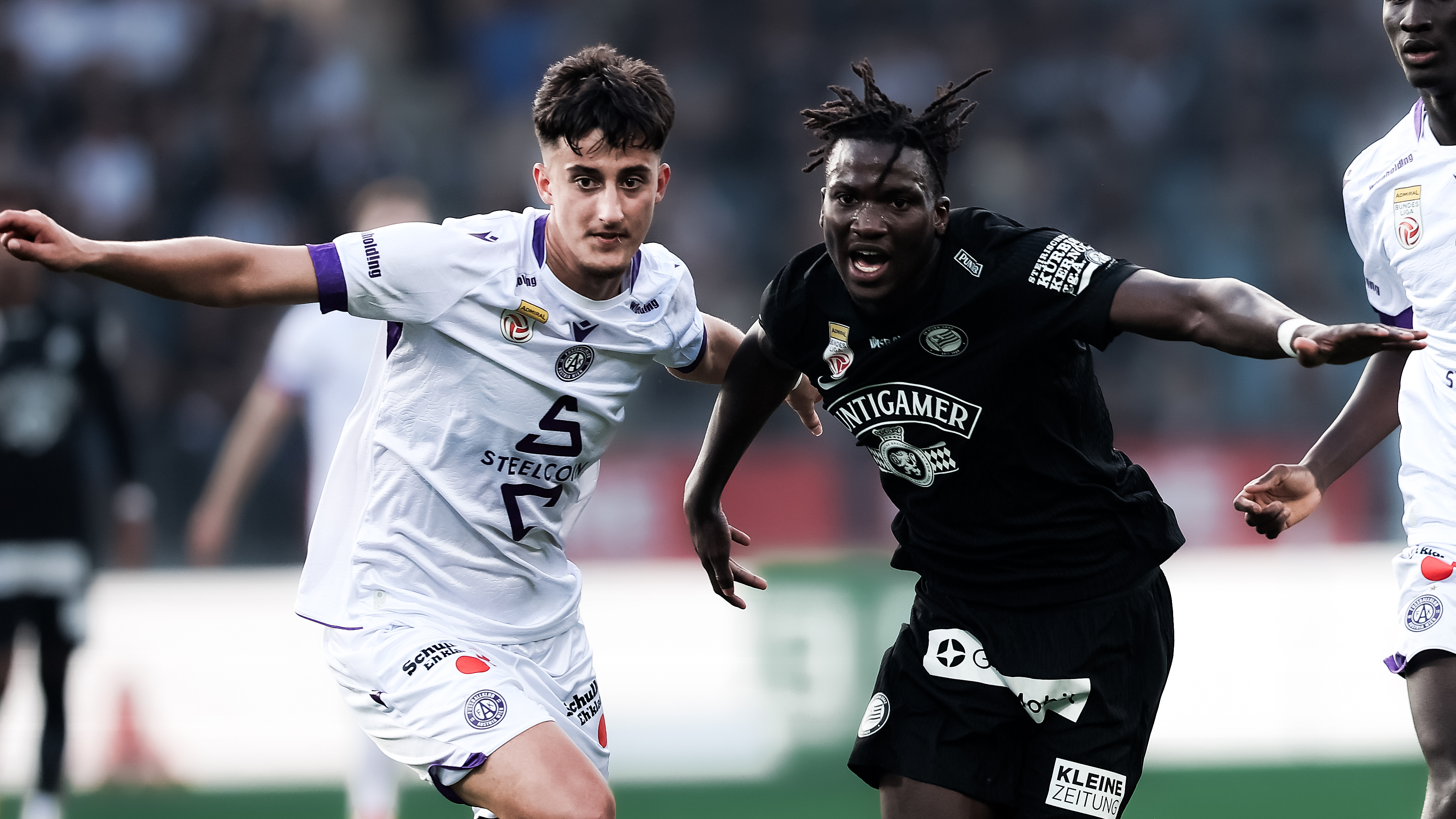 Ein Spieler in schwarz und ein Spieler in weiß kämpfen um einen Ball. Beide haben eine Hand ausgestreckt.