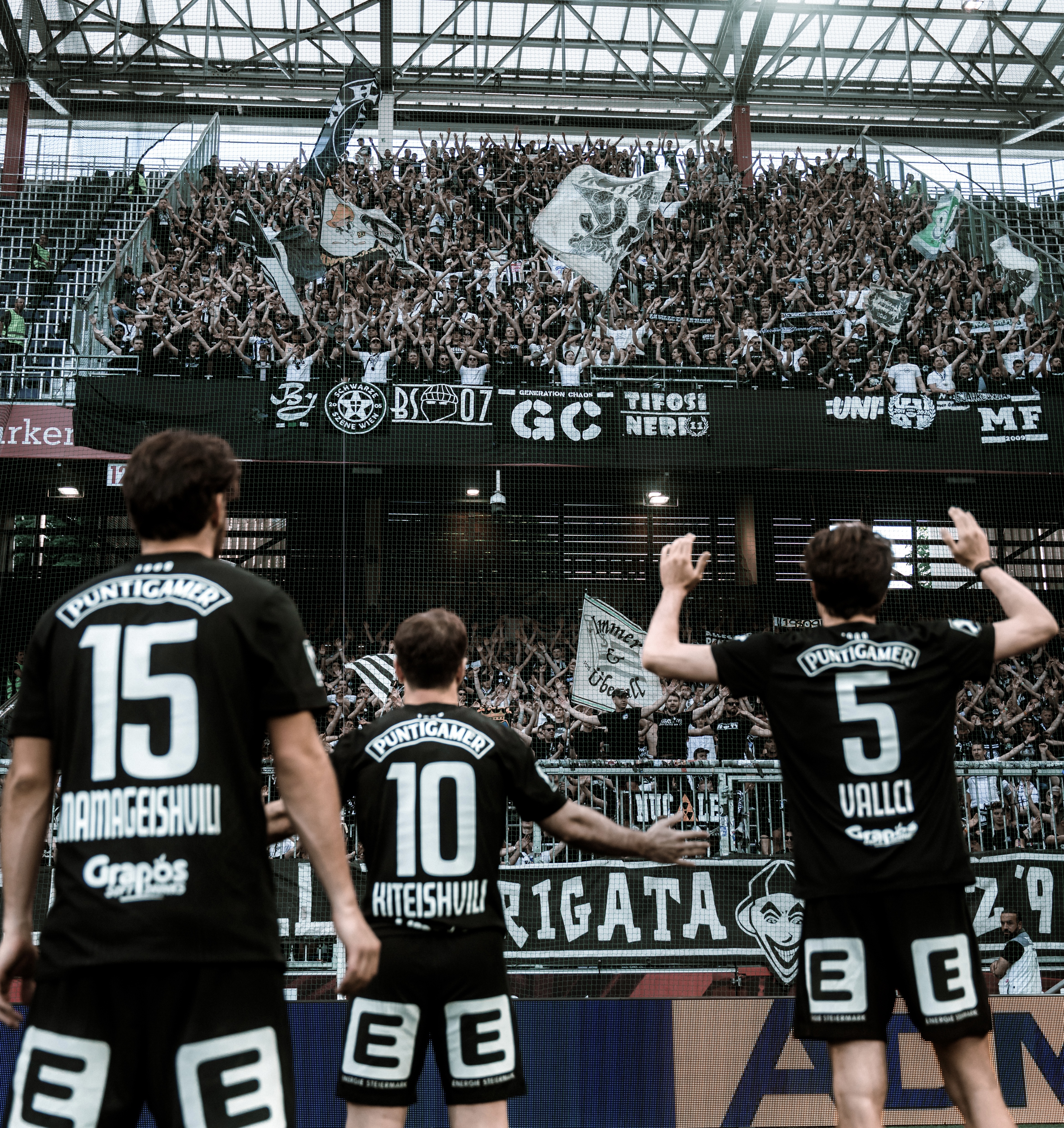 Drei Spieler stehen vor vielen Fans und haben die Hände in der Luft.