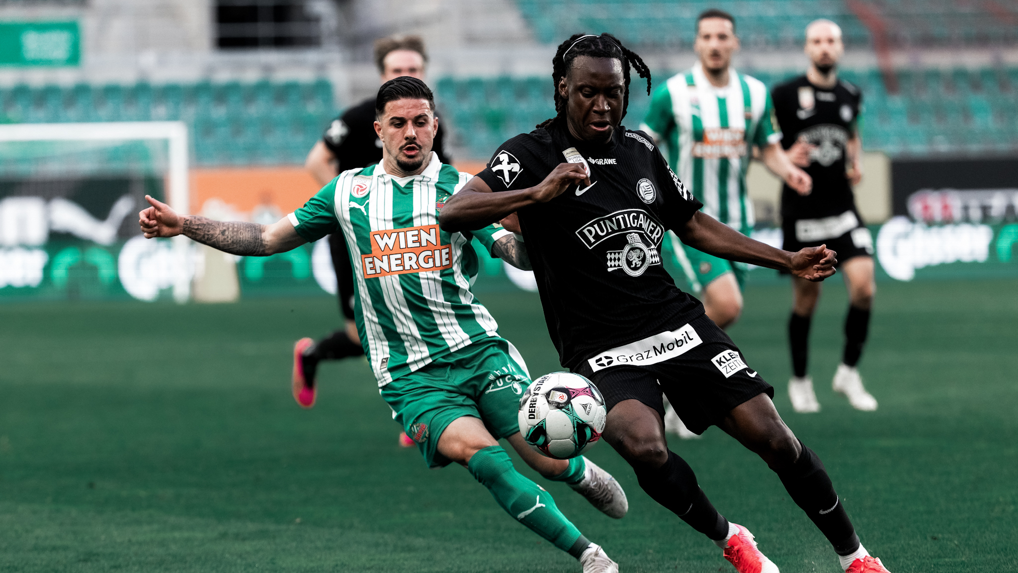 Ein Spieler in schwarz und ein Spieler in grün-weiß kämpfen um einen Ball.