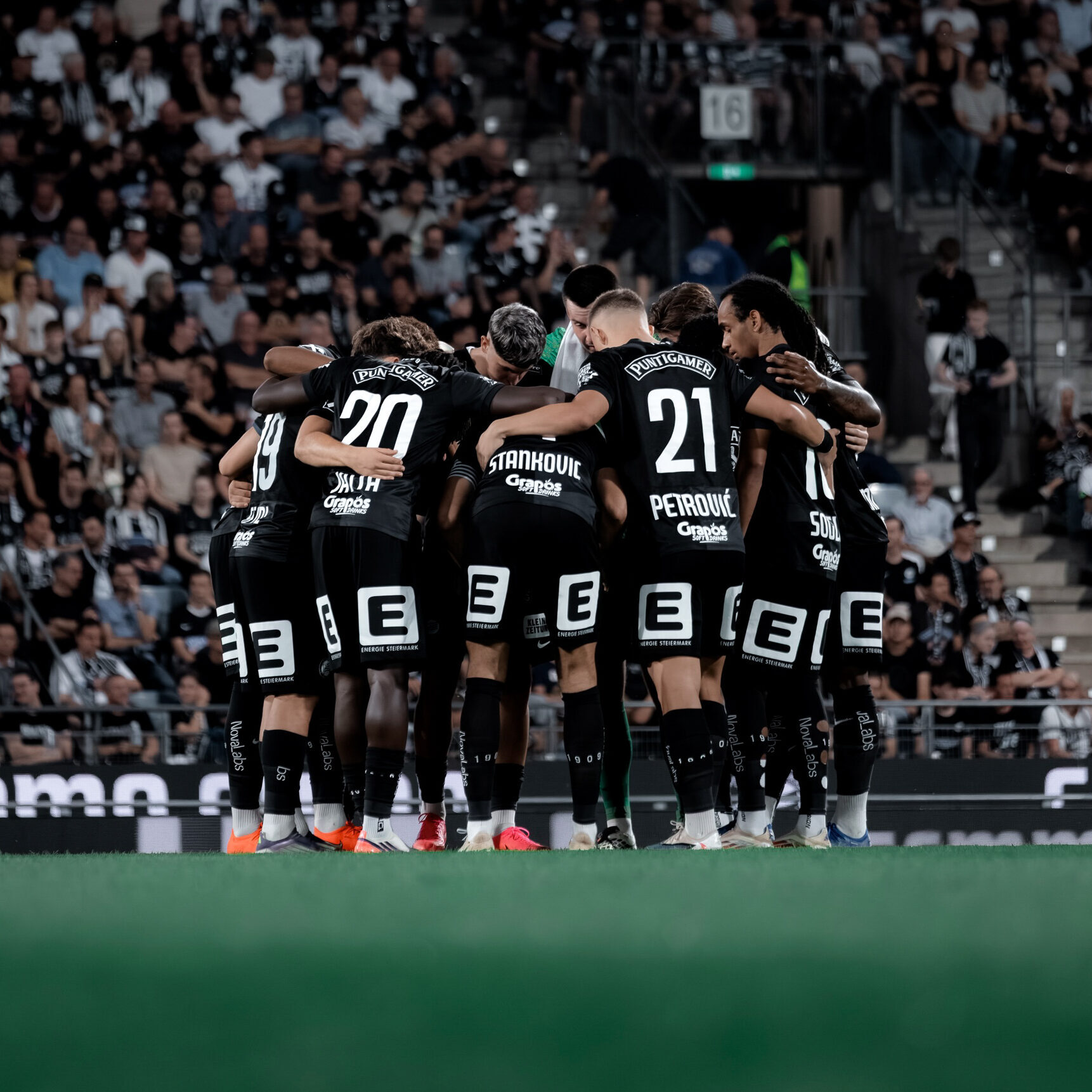 Viele Spieler in schwarzen Trikots stehen im Kreis und umarmen sich.