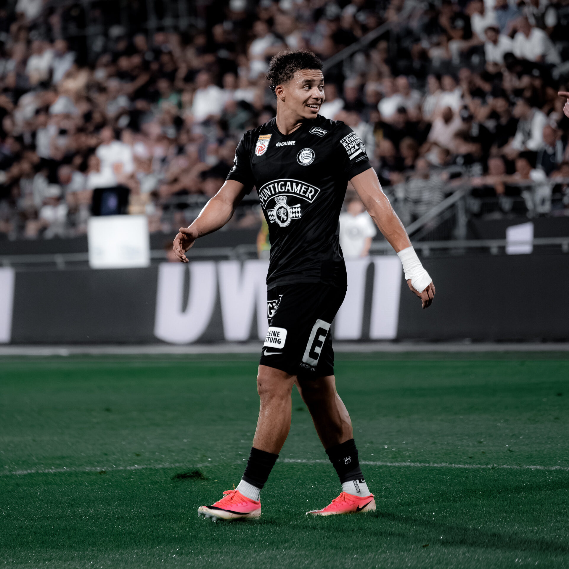 Ein Spieler in einem schwarzen Trikot geht auf einem grünen Rasen und schaut nach rechts.