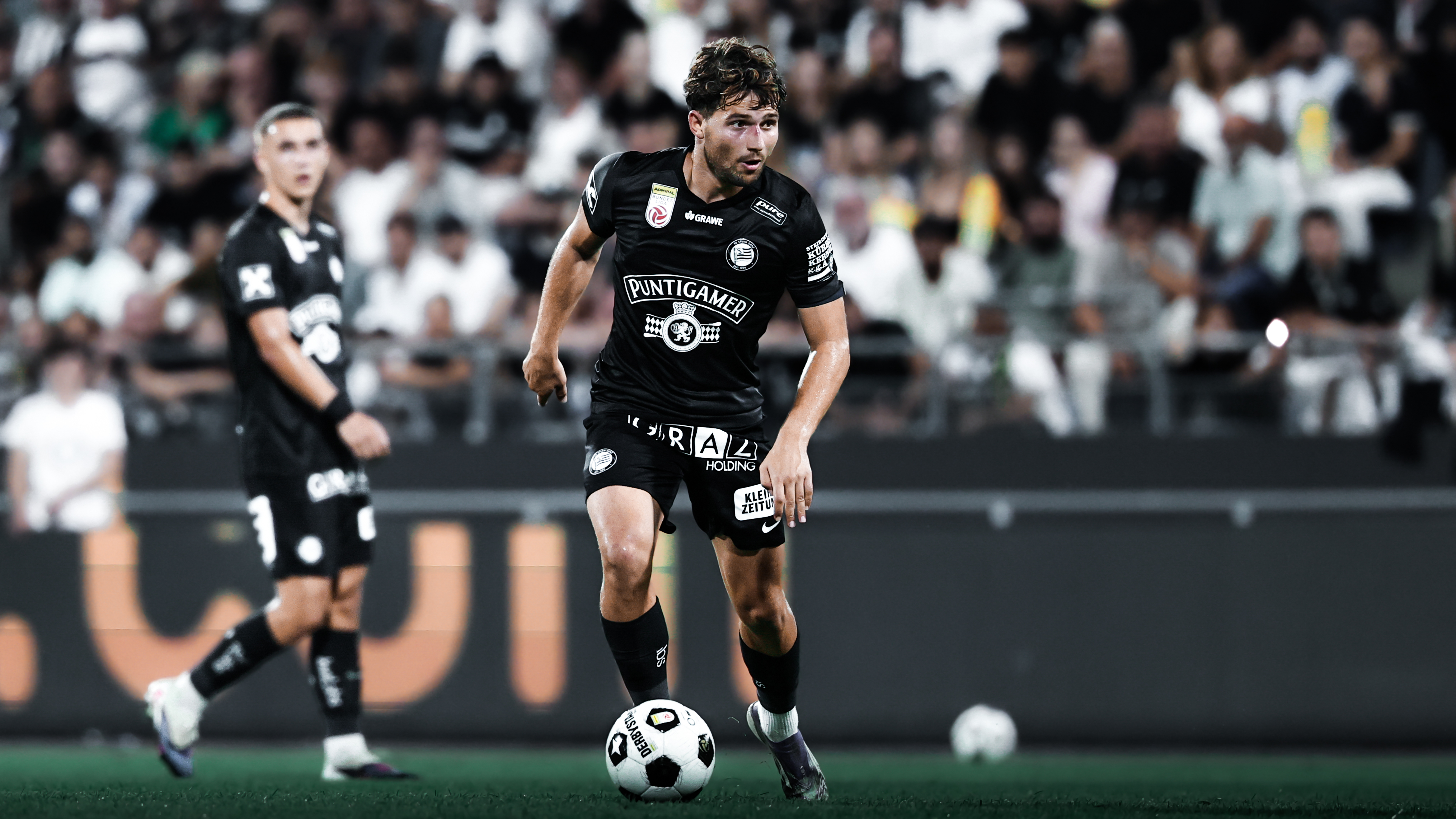 Ein Spieler in einem schwarzen Trikot führt einen weißen Ball am Boden.