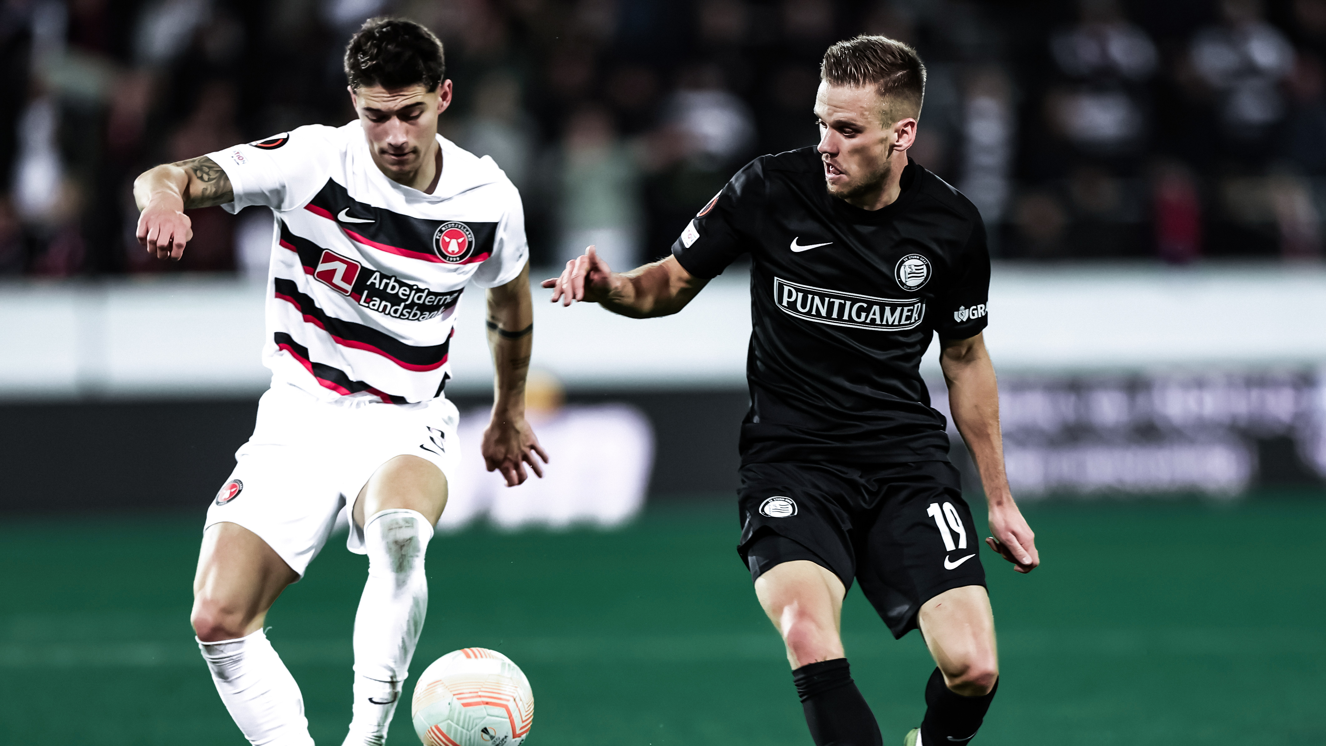 Zweikampf um den Ball von einem Spieler in schwarz und einem in weiß