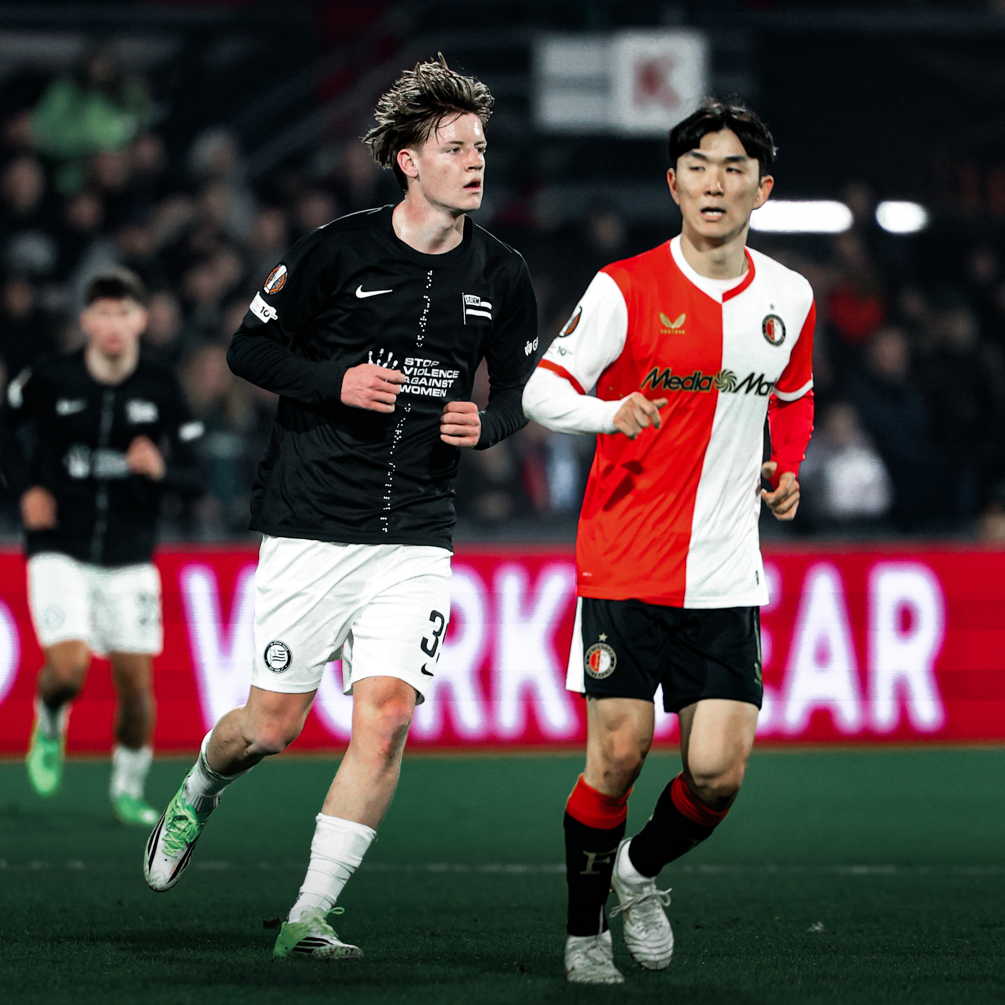 Ein Spieler in einem schwarzen und ein Spieler in einem rot weißen Trikot laufen.