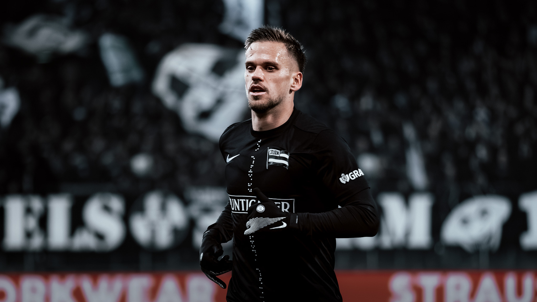 Ein Spieler in einem schwarzen Trikot und mit schwarzen Handschuhen läuft im Stadion.