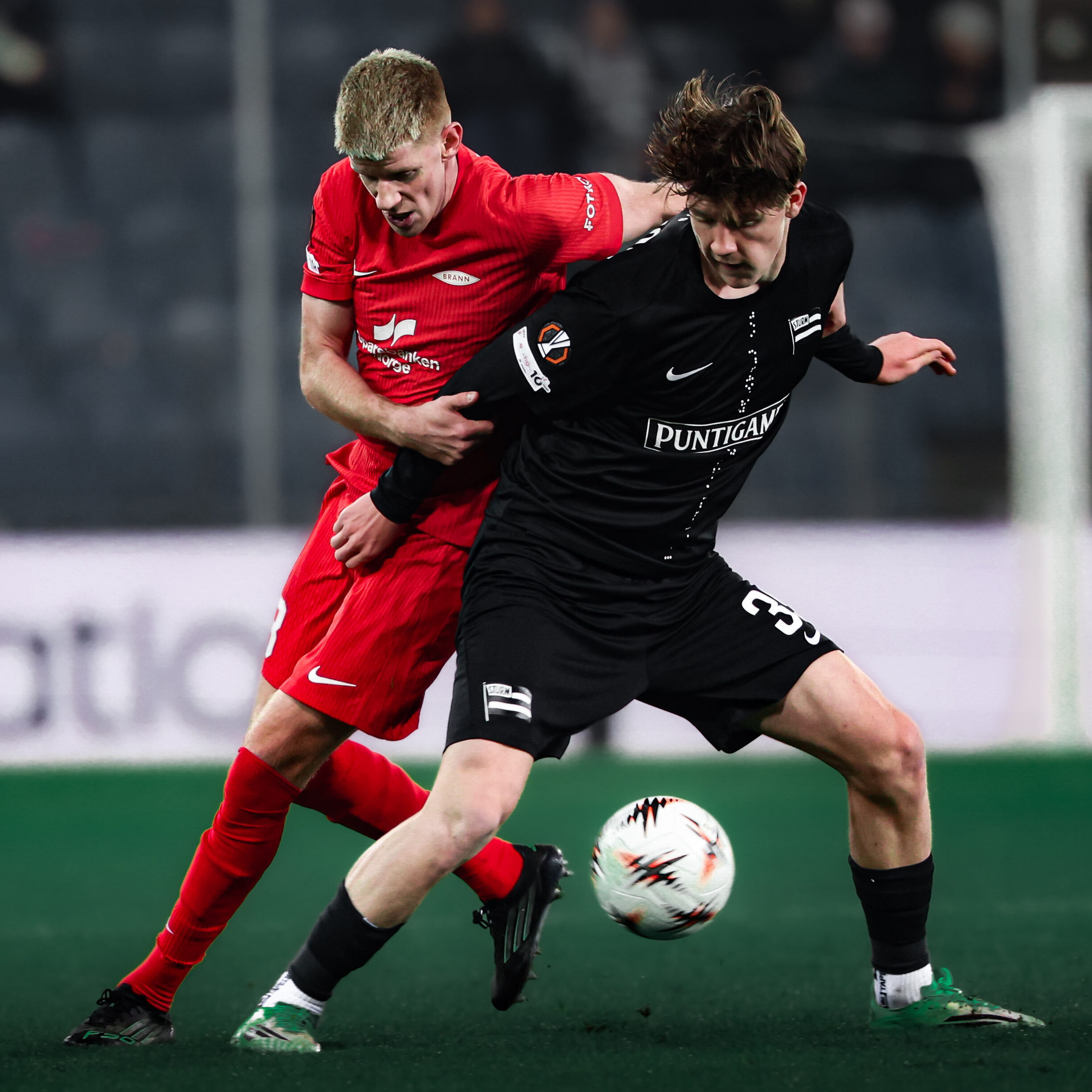 Ein Spieler in einem schwarzen und ein Spieler in einem roten Trikot im Zweikampf.